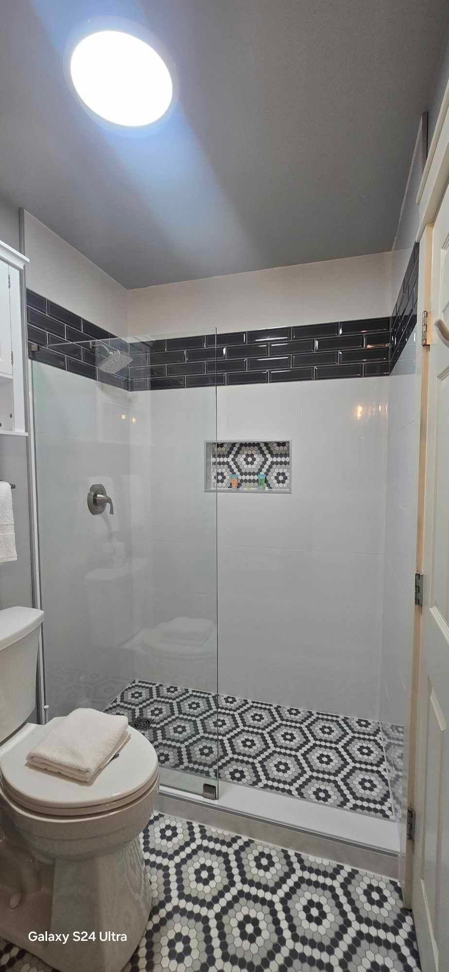 Bathroom with black and white hexagon floor tiles, glass shower, and skylight.