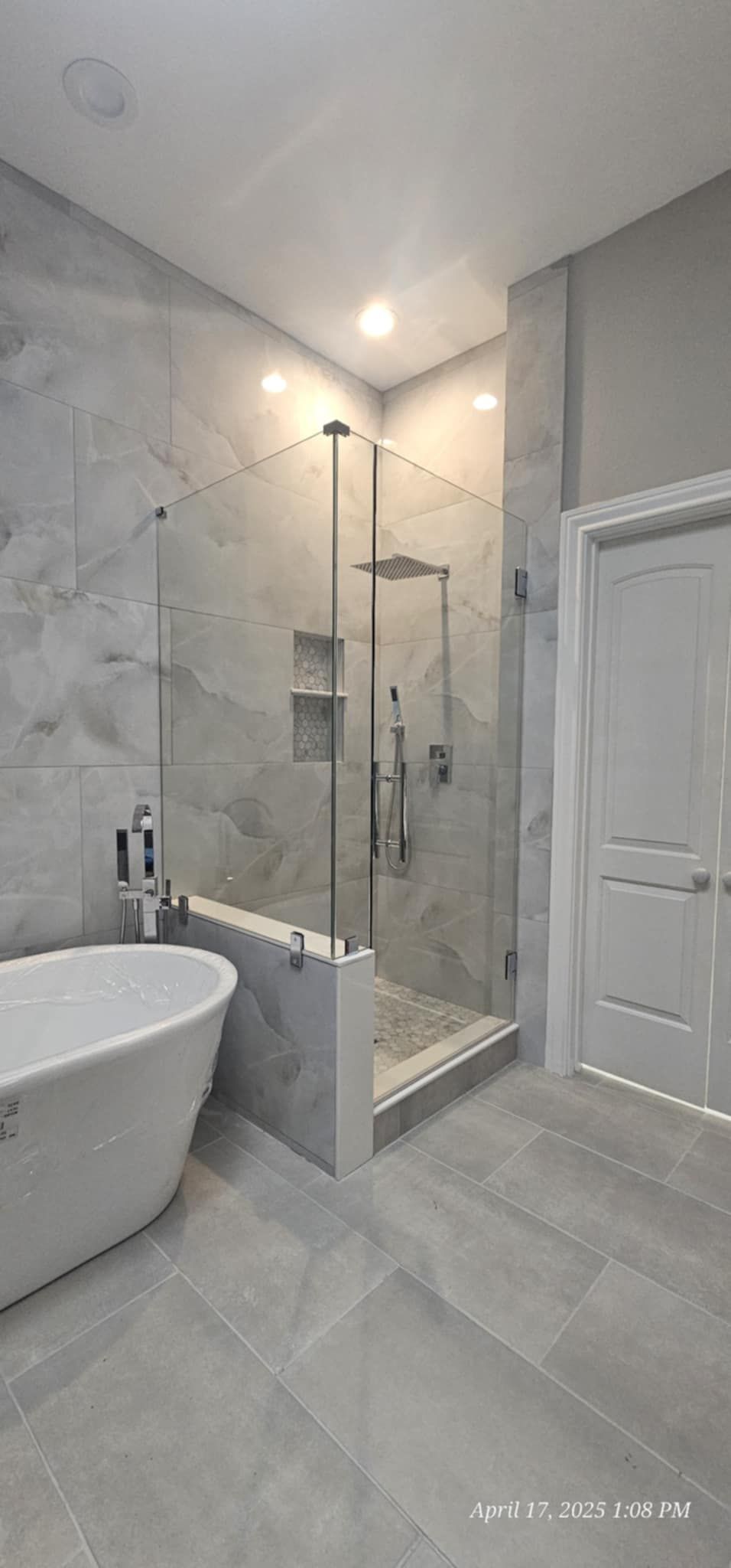 Bathroom with a freestanding tub, glass shower, and gray tile.