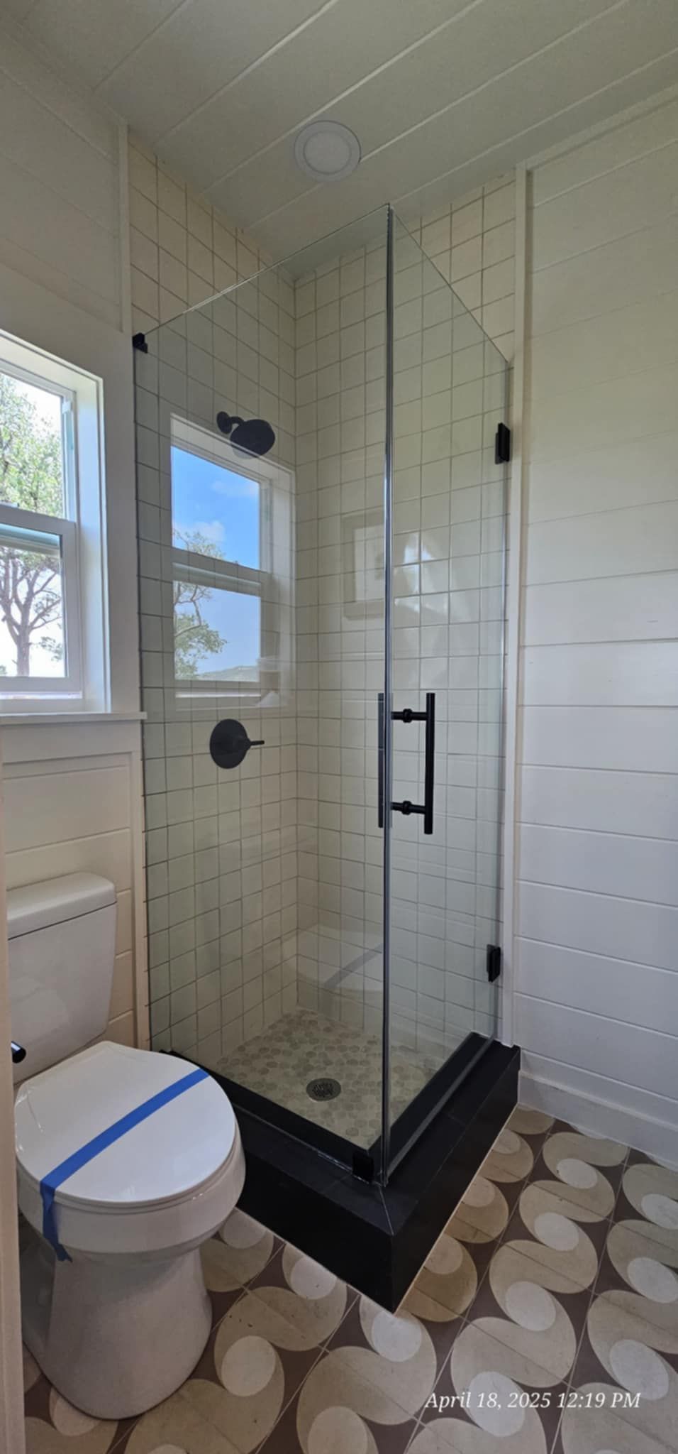 Bathroom with glass shower, white walls, and wood-look floor. Toilet on left.