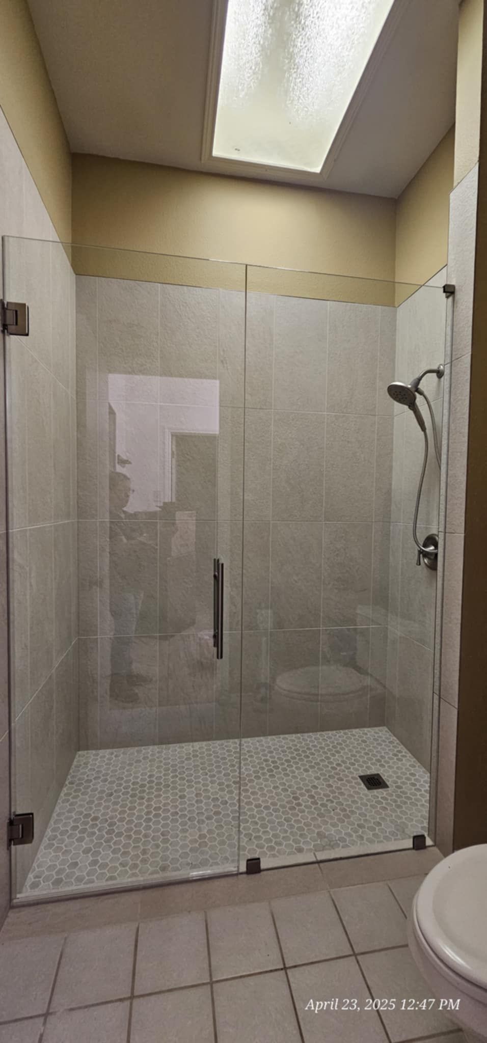 A modern, glass-enclosed shower with a pebble-stone floor in a bathroom. Natural light enters through a ceiling window.