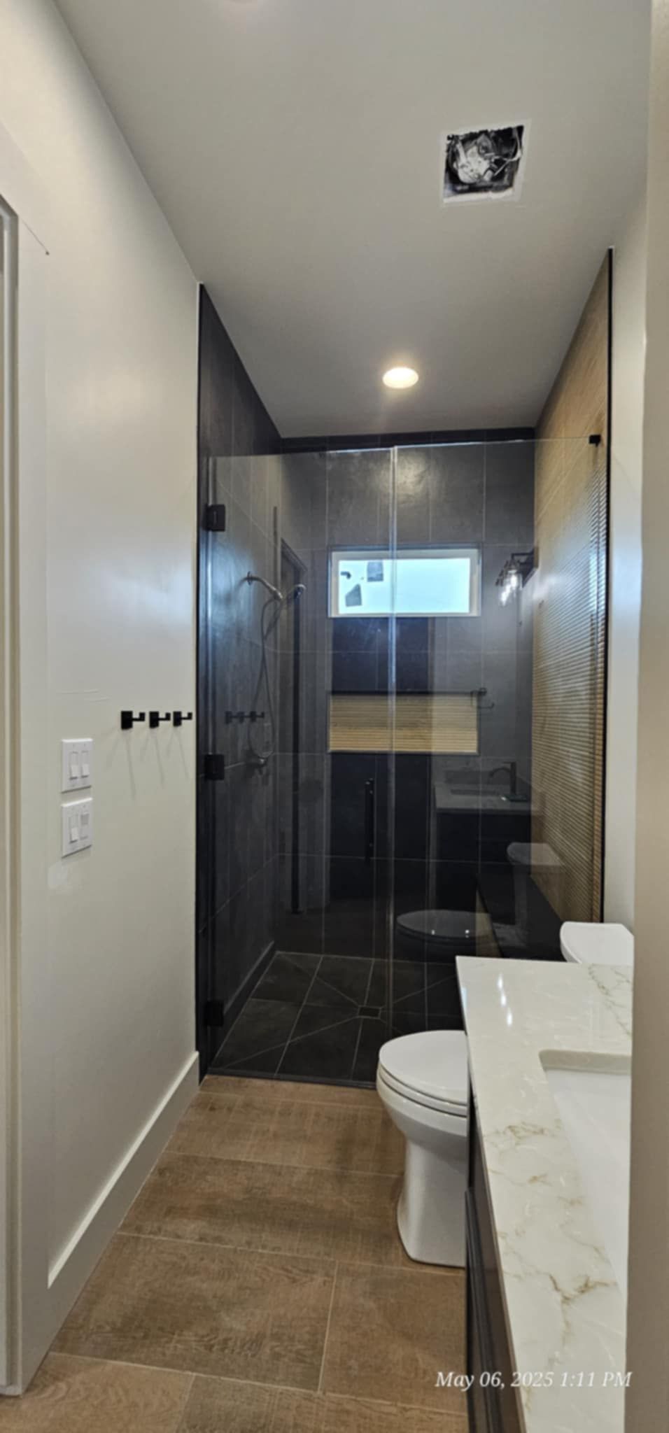 Narrow bathroom with a shower, toilet, and vanity. The walls are light and the floor is brown tile.