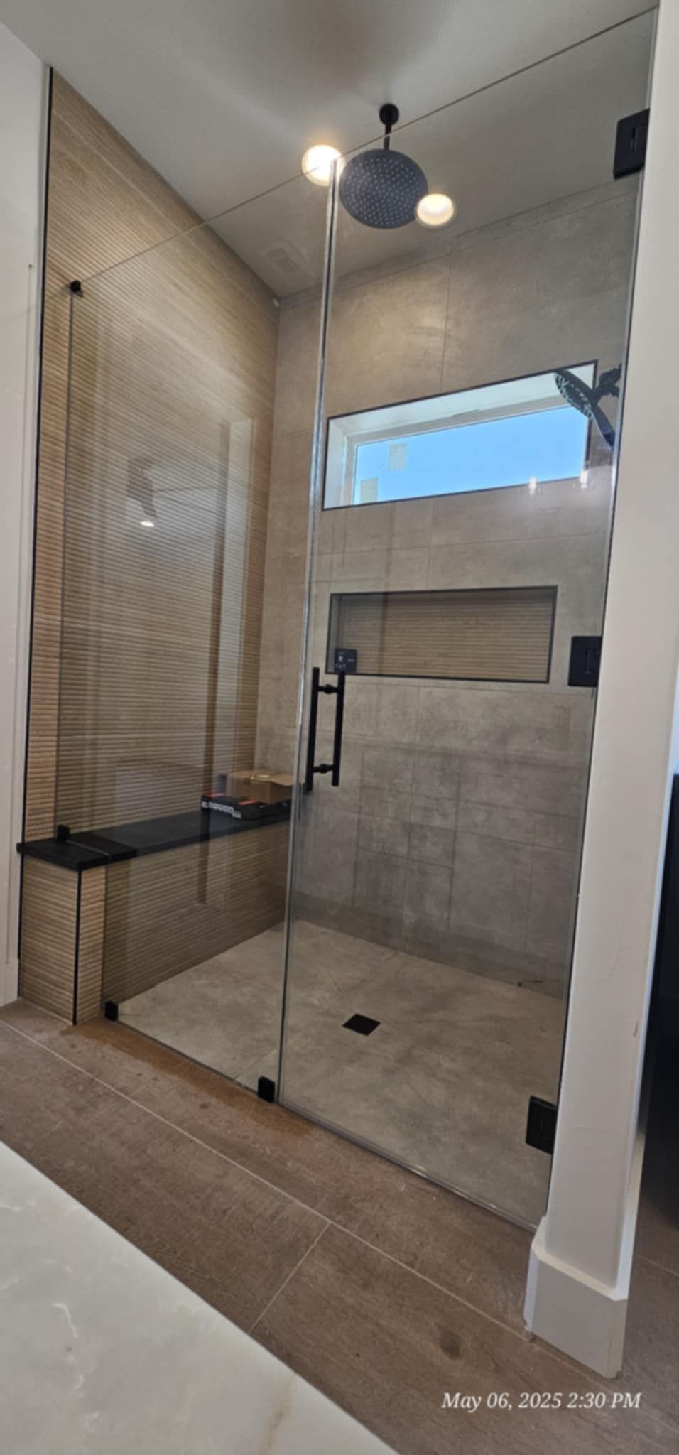 Modern shower with glass walls, tiled interior, bench, and window.