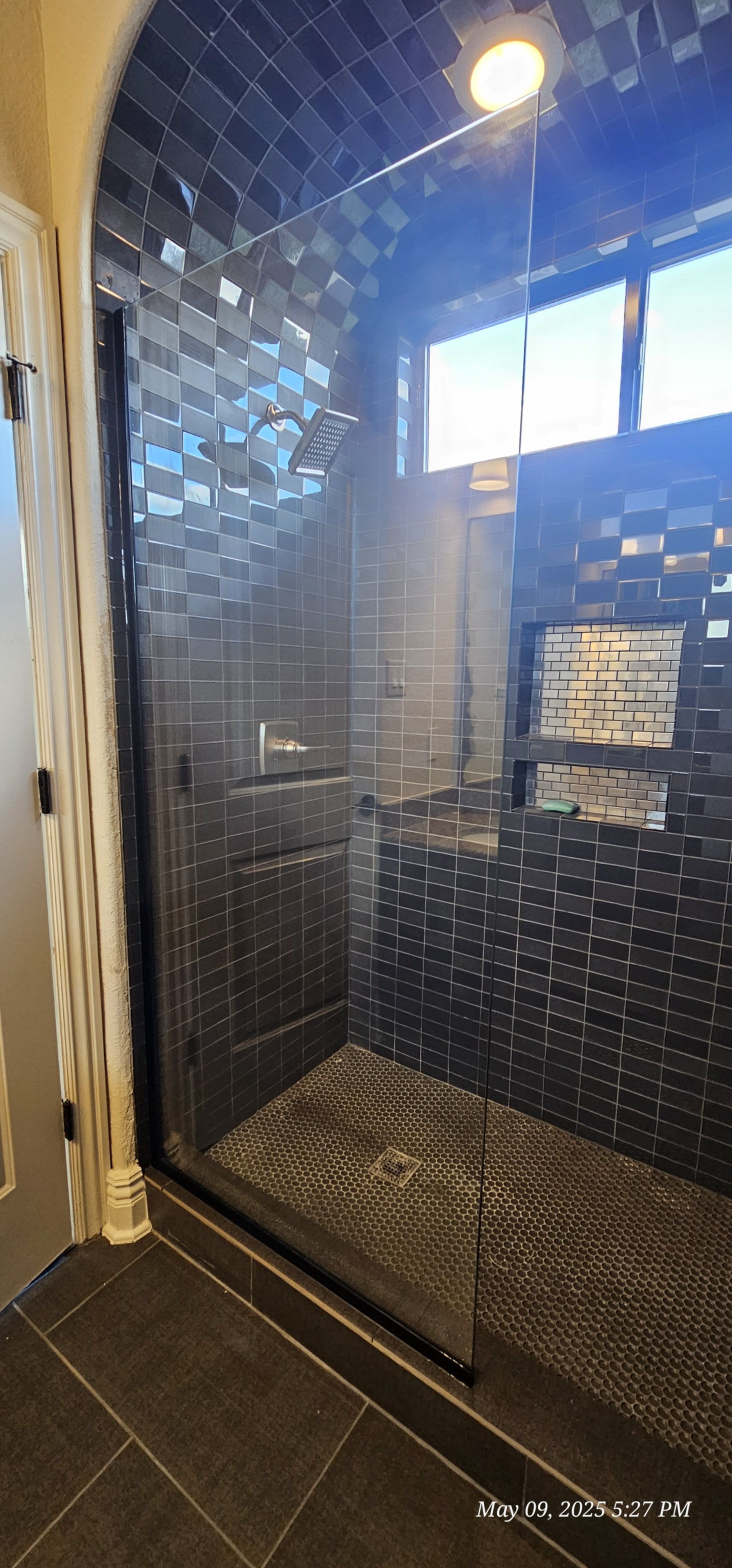 A modern bathroom shower with dark, textured tiles and a glass door.