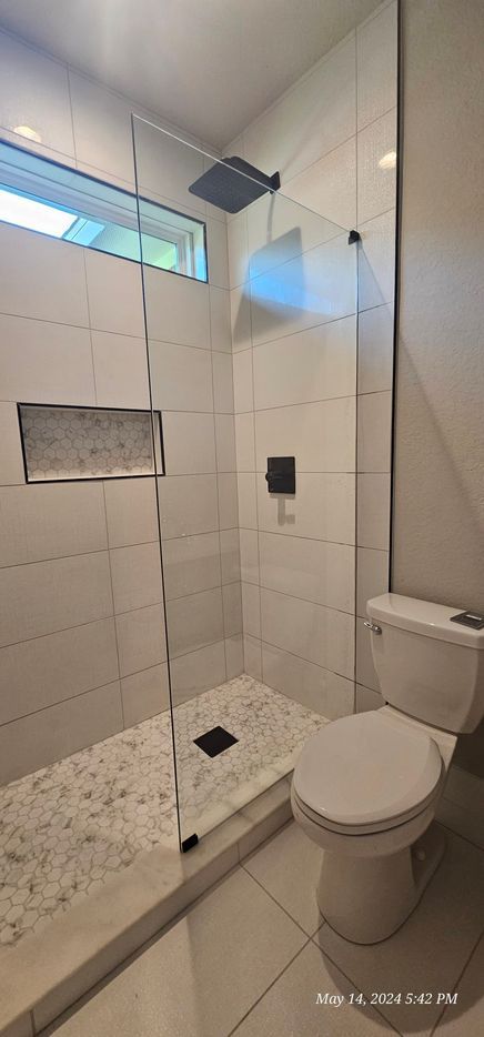 A modern bathroom with a glass shower, white tiled walls, and a toilet.