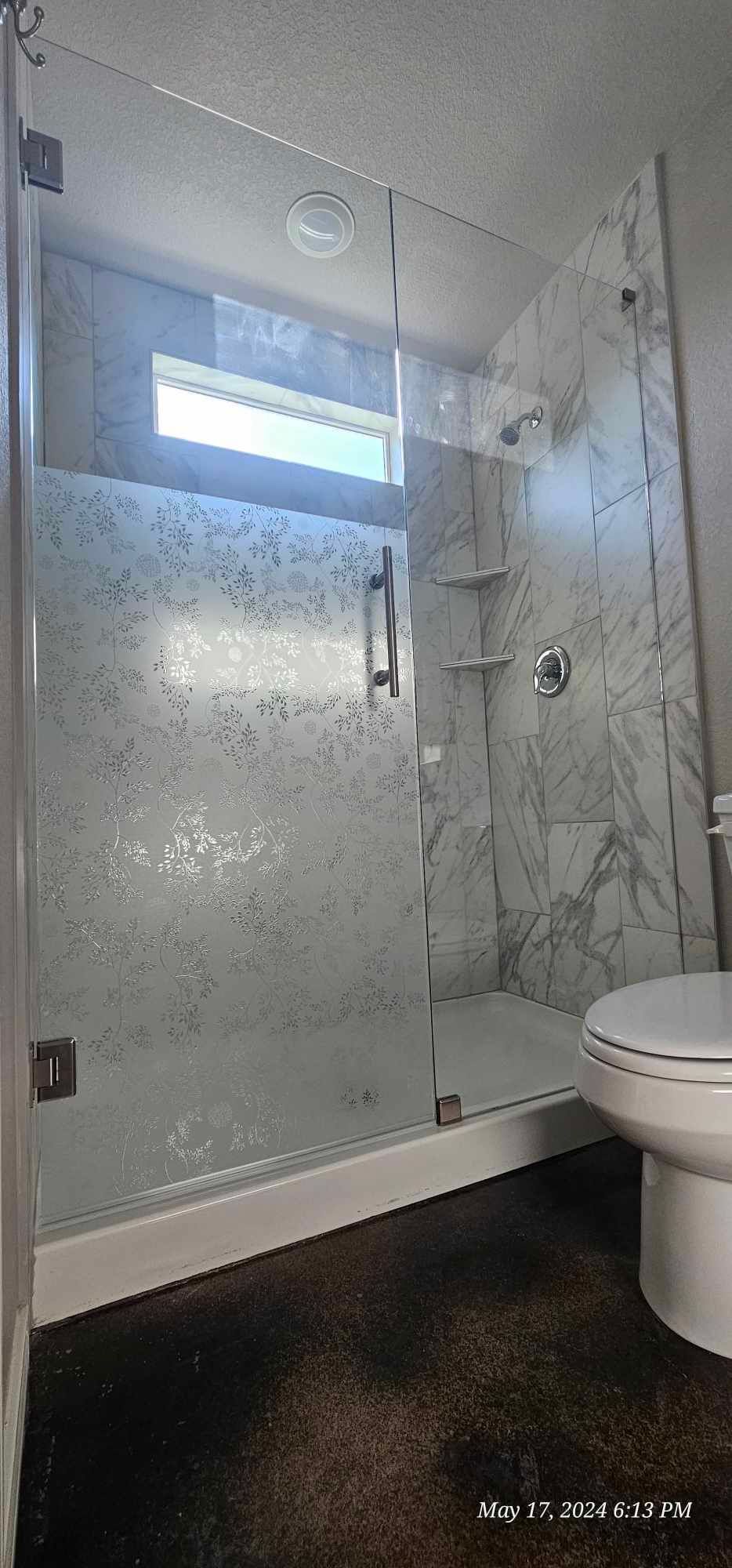 Modern bathroom with a glass shower enclosure and marble walls, next to a toilet.