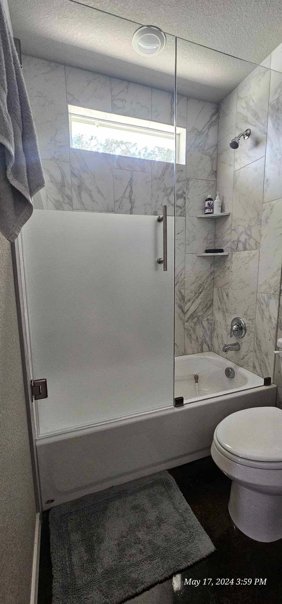 Bathroom with a tub, frosted glass shower door, marble tile walls, and a toilet.