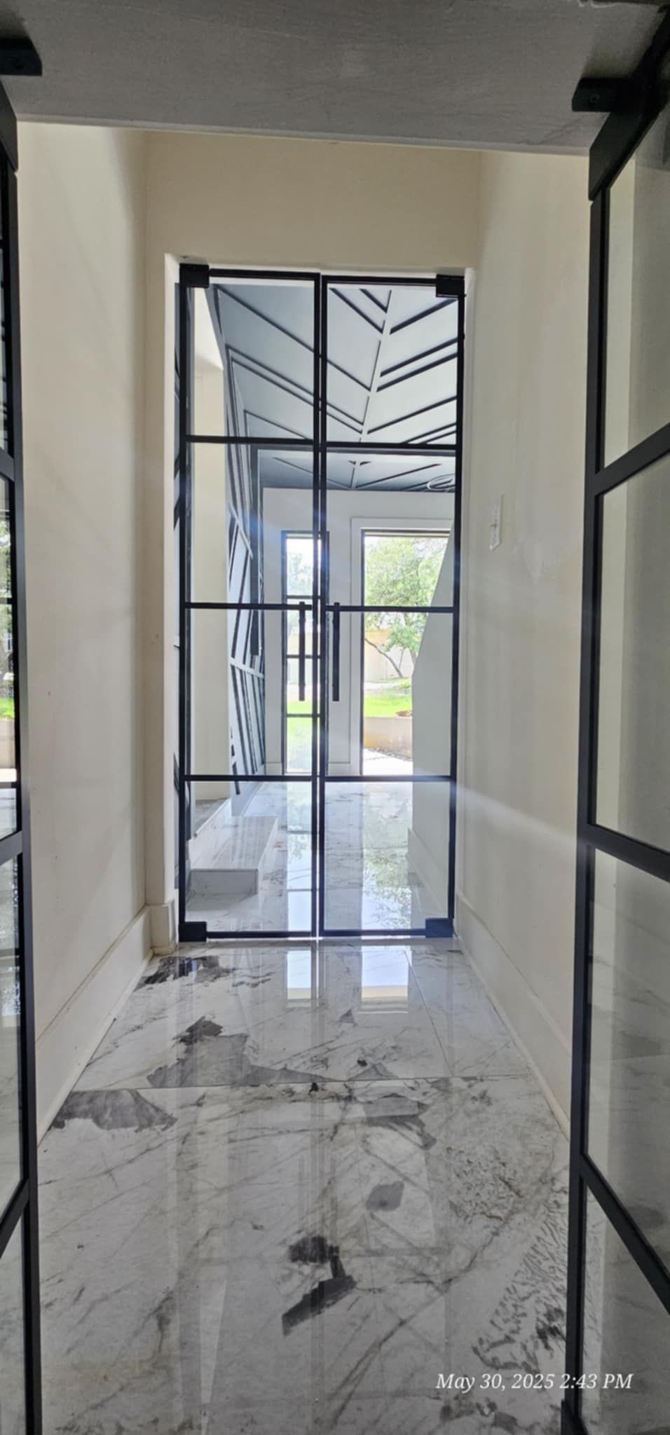 Hallway with glass doors and black framing leading to a garden.