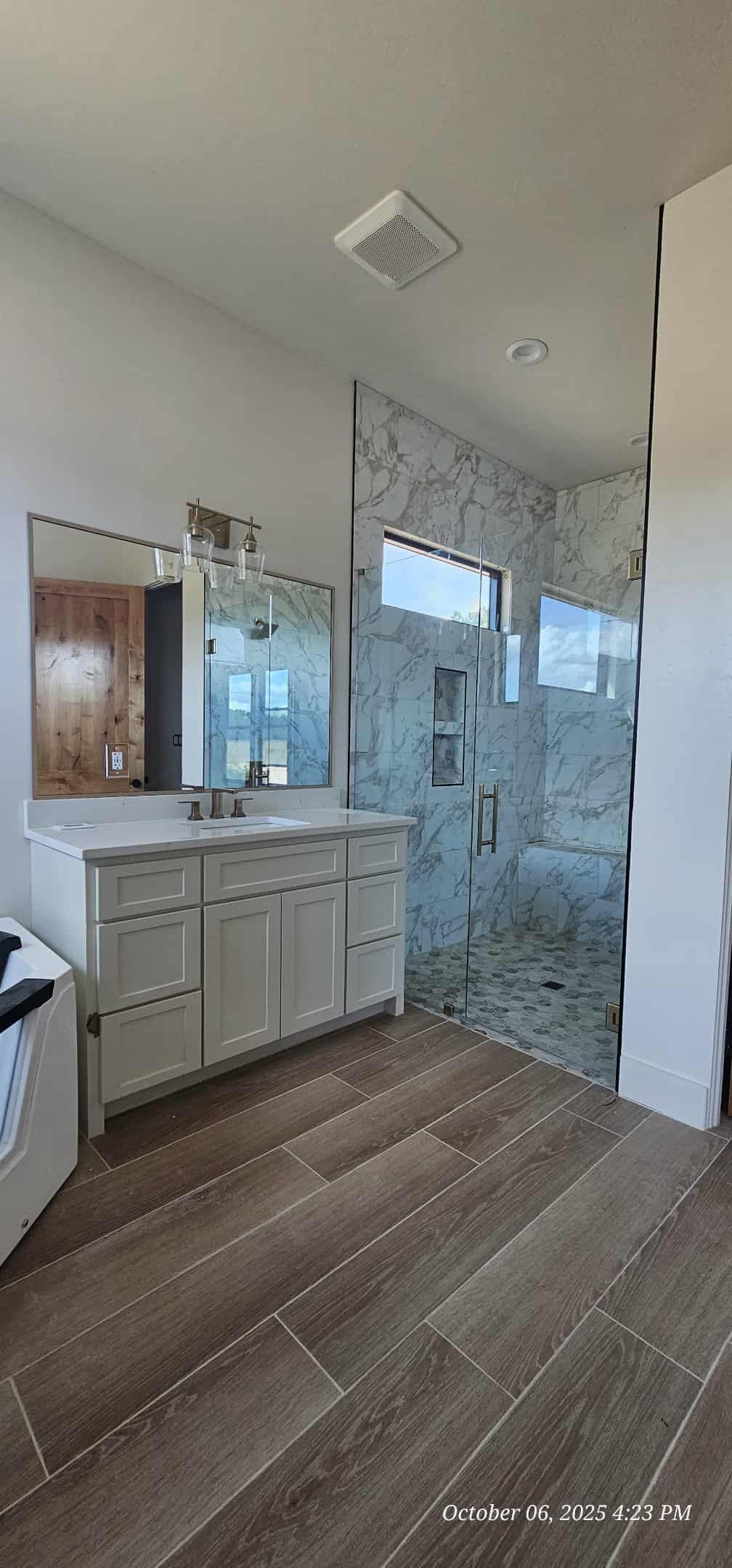 Bathroom with a vanity, large mirror, walk-in shower with glass doors, and wood-look flooring.