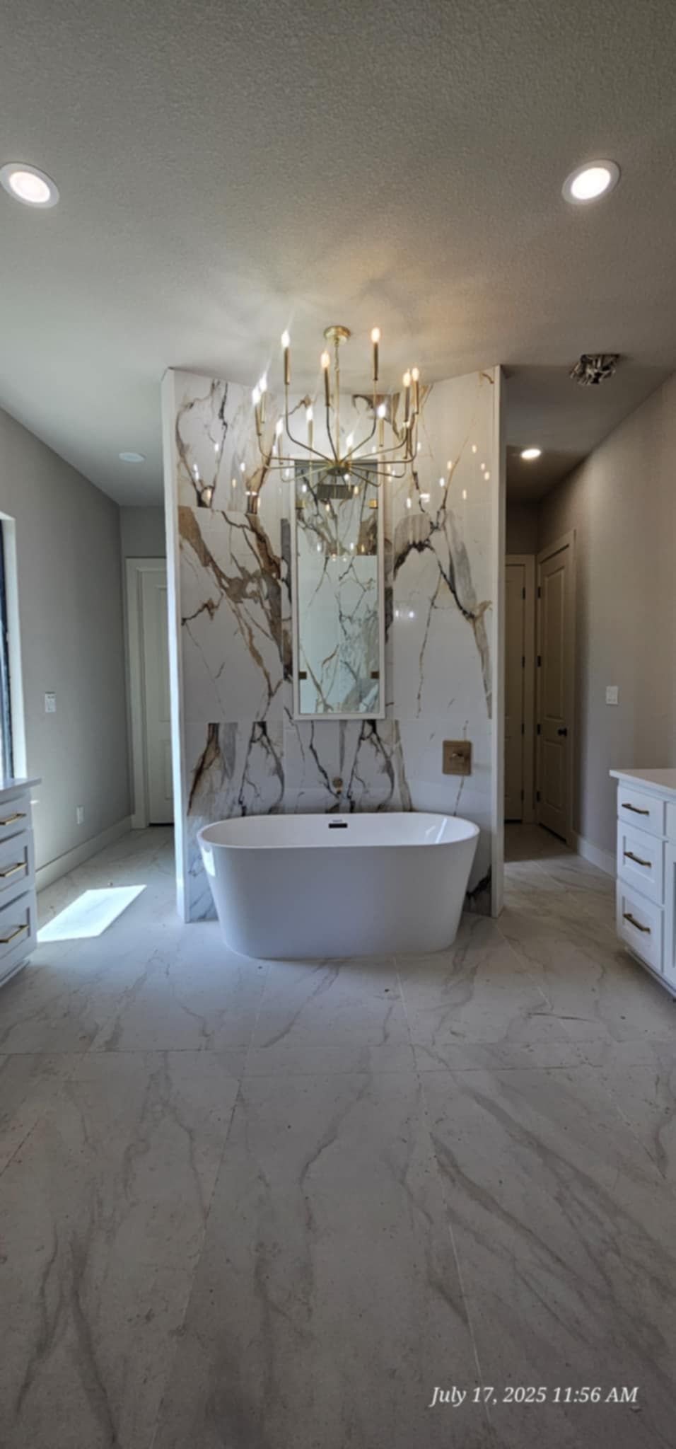 A modern bathroom with a freestanding tub, marble accent wall, and chandelier.