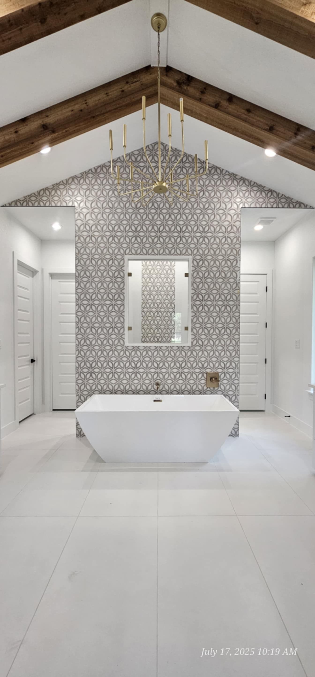 White bathroom with geometric patterned accent wall, centered tub, wooden beams.