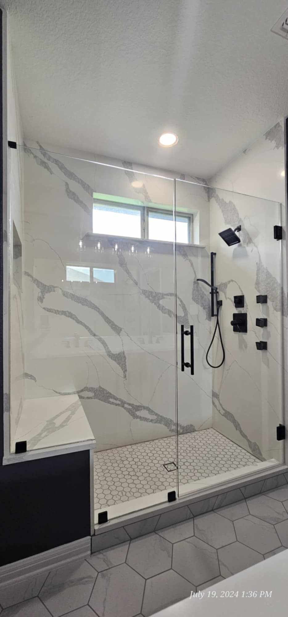 Modern shower with marble-like wall tile and glass enclosure, black fixtures.