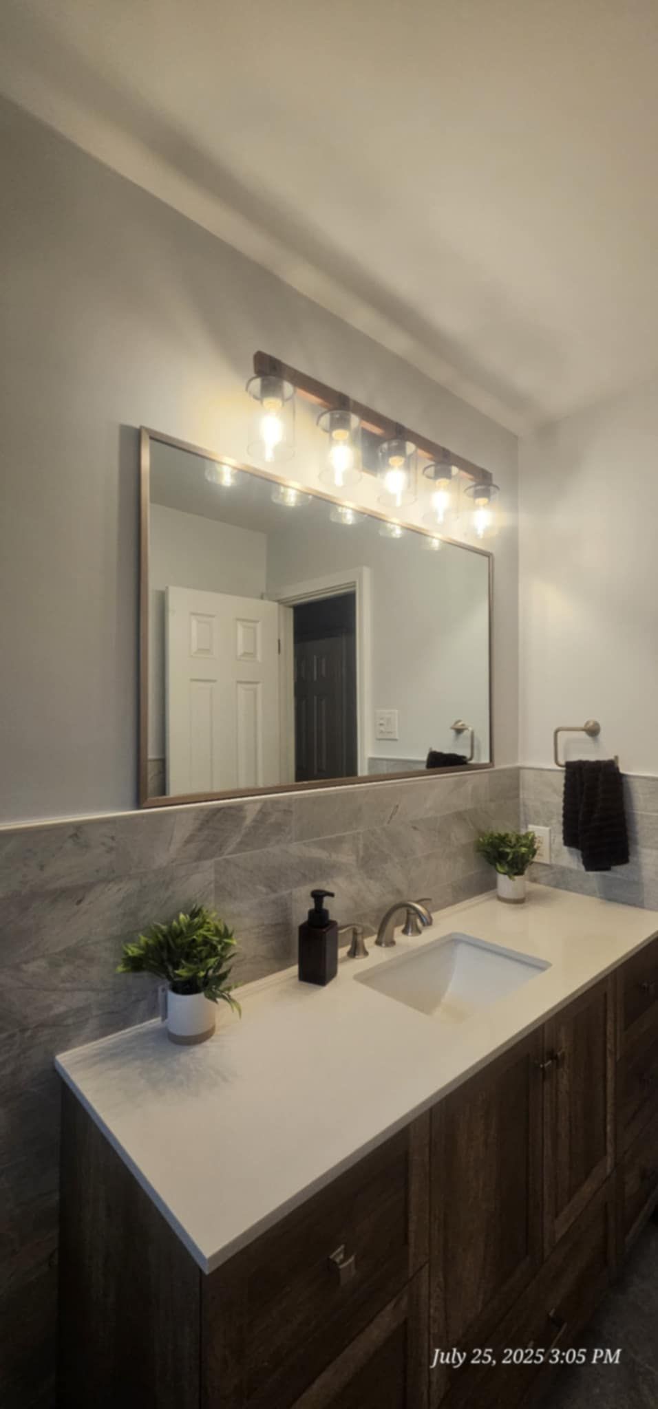 Bathroom with a large mirror, vanity, and lighting fixture. Gray walls and a white countertop.