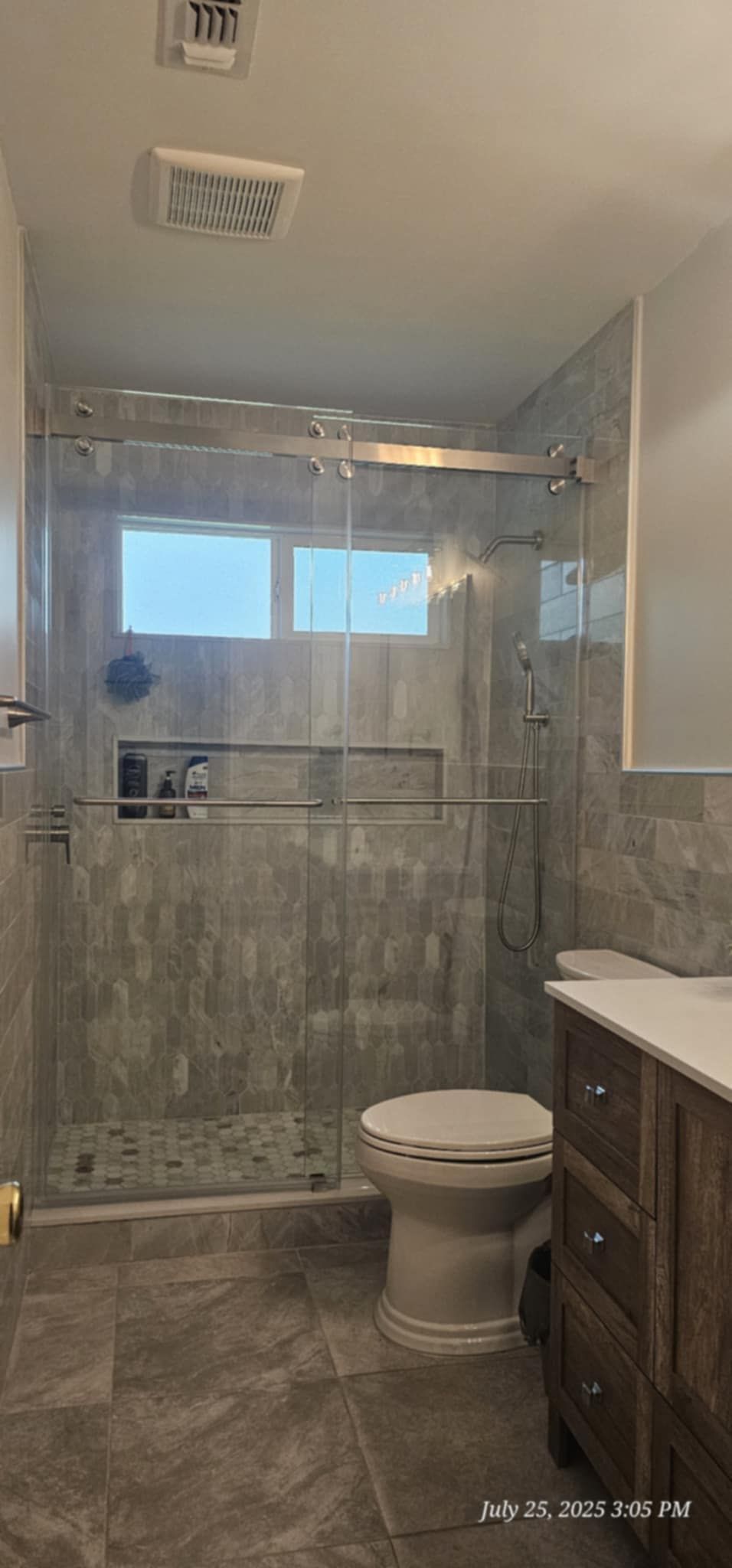 Bathroom with a gray tiled shower, toilet, and wooden vanity.