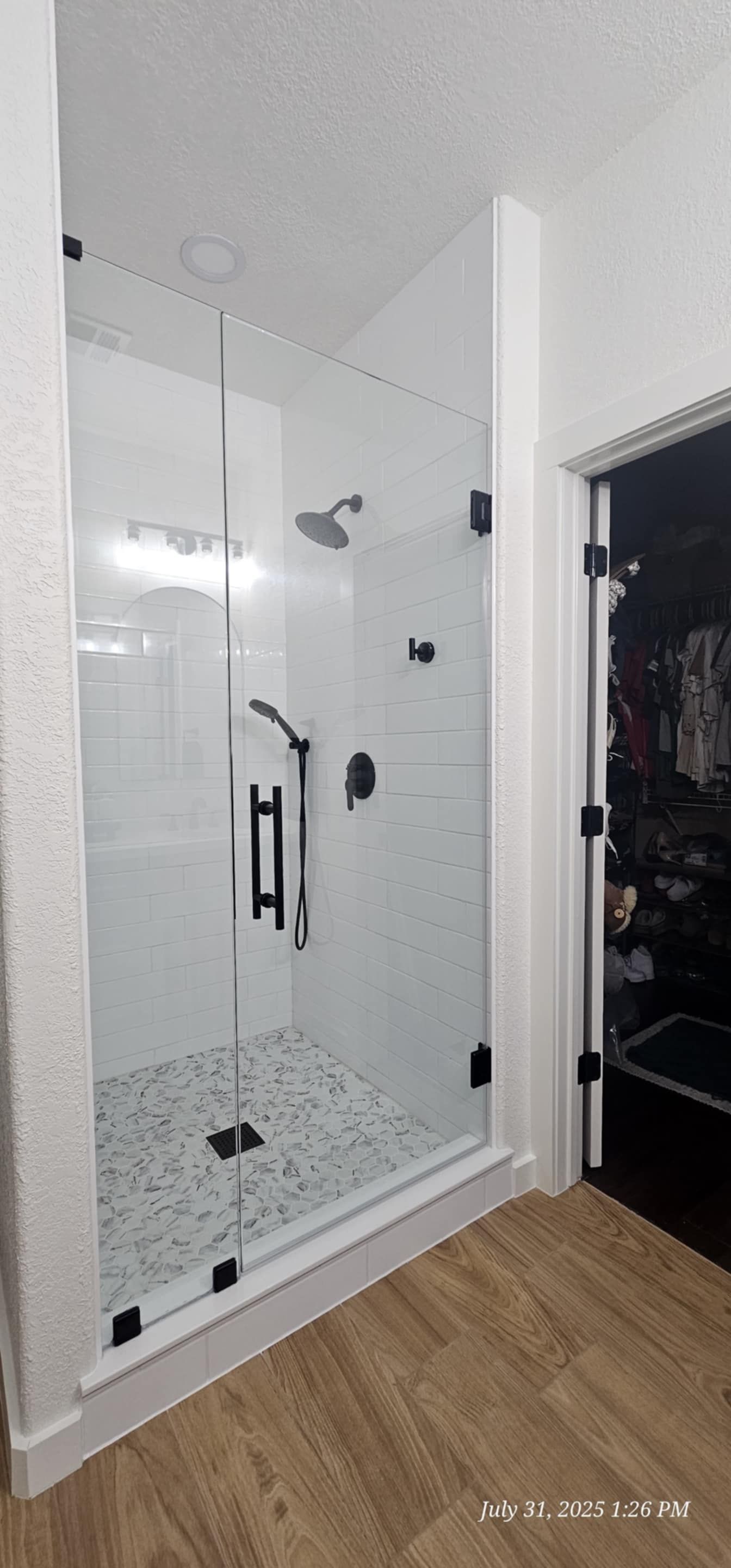 A modern shower with clear glass doors and black fixtures. The floor is tiled with small white and gray stones.