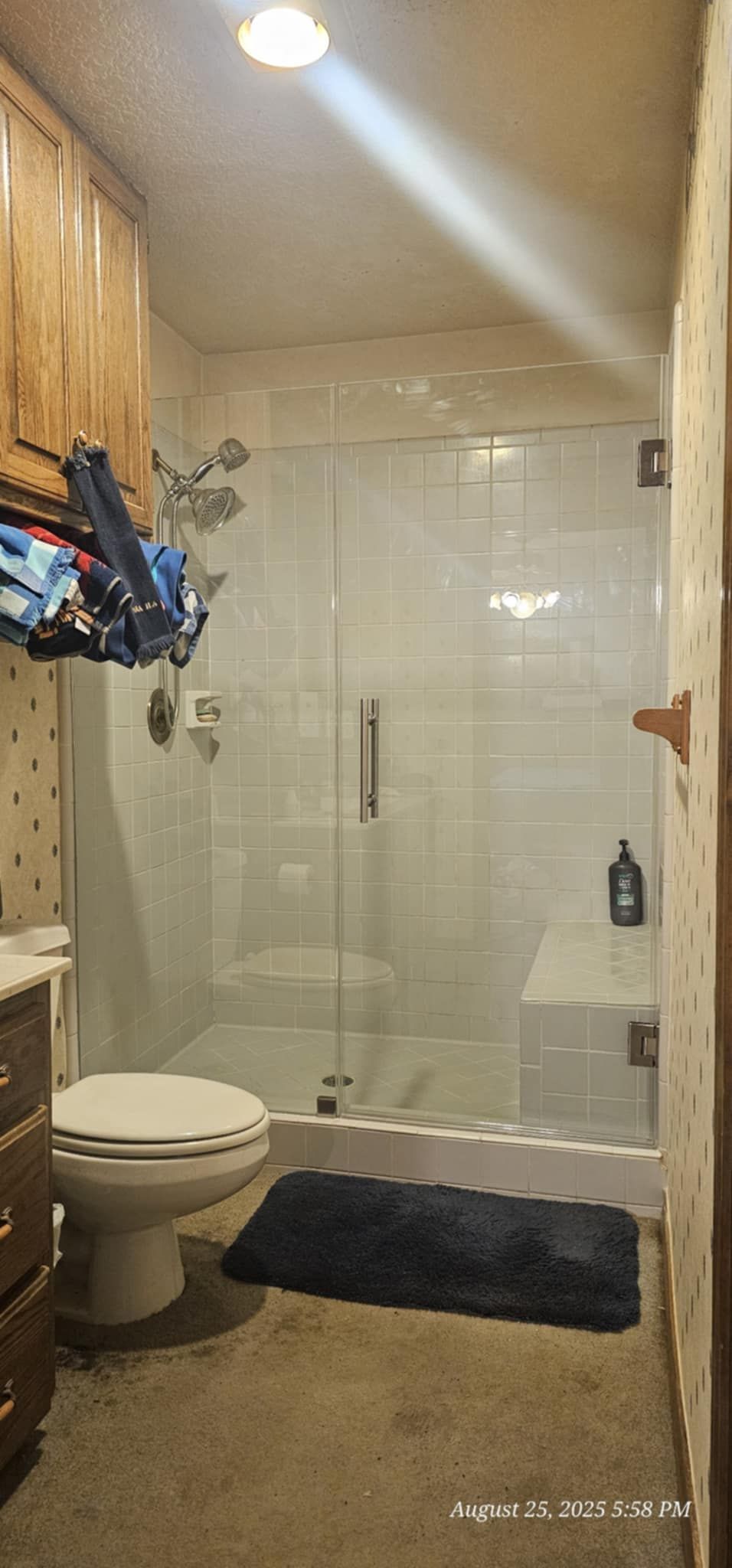 Bathroom with a glass shower, toilet, and wooden cabinets. A blue rug is on the floor.