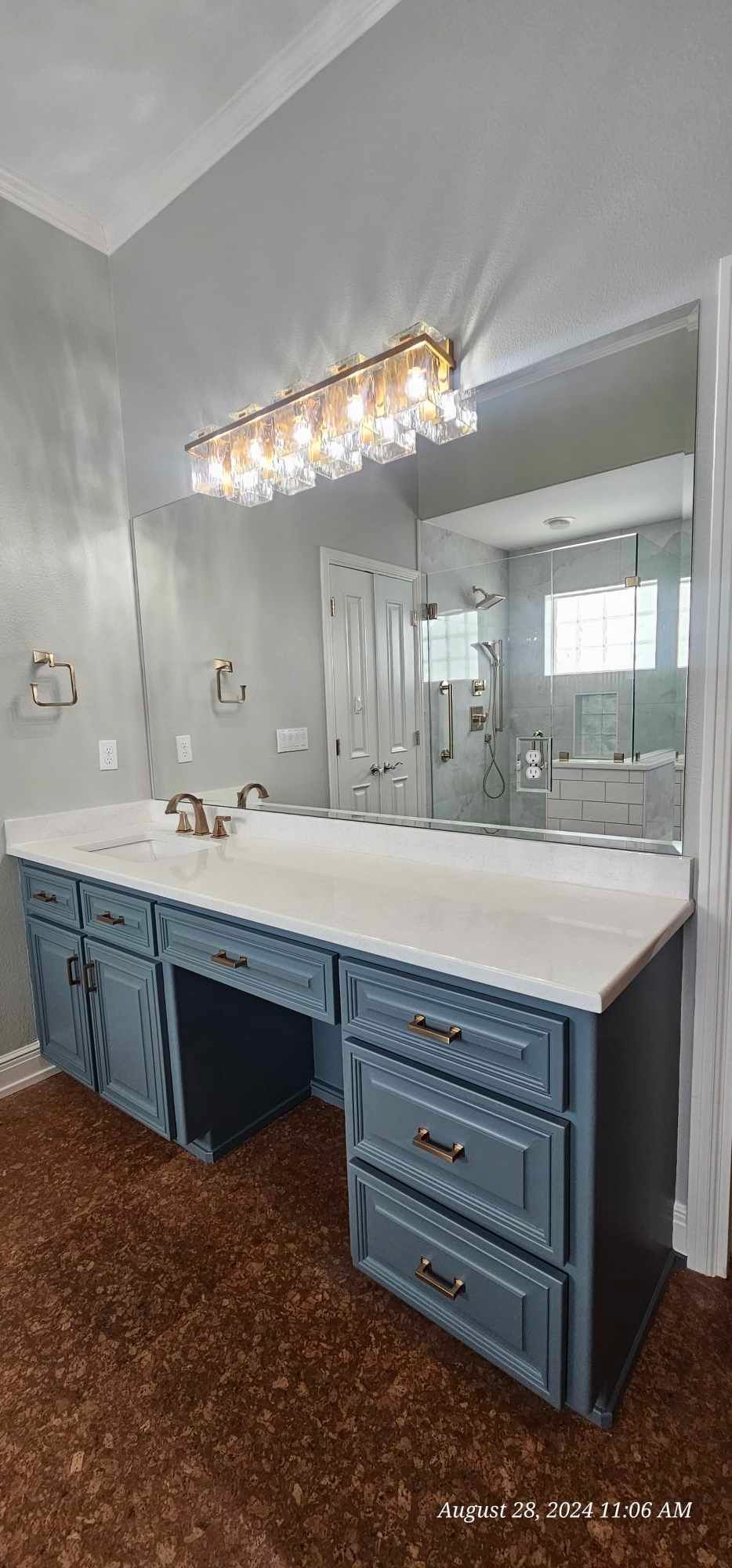 Bathroom with blue vanity, white countertop, large mirror, and decorative light fixture.
