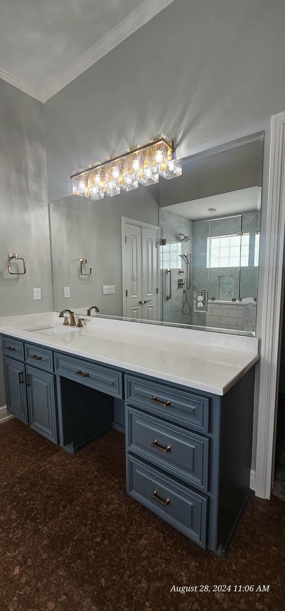 Bathroom with blue cabinets, white countertop, large mirror, and decorative light fixture.