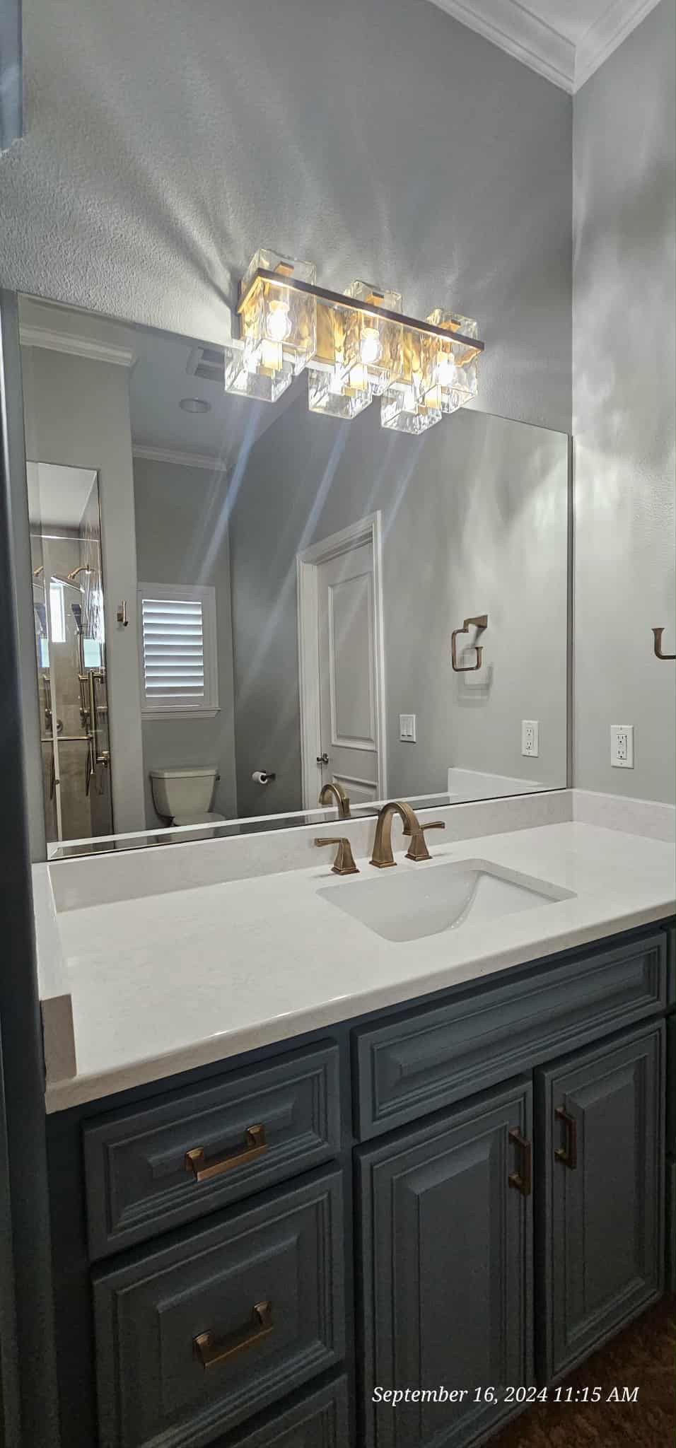 Bathroom with a large mirror, vanity with gray cabinets, white countertop, and gold hardware.