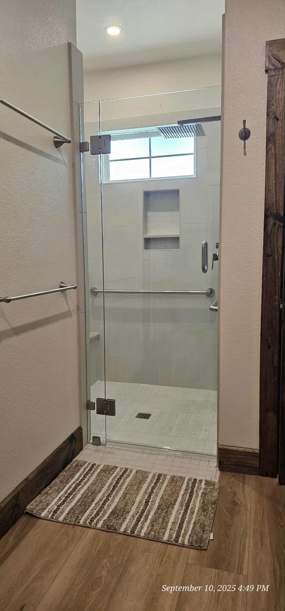 A bathroom with a clear glass shower door. There's a small rug on the floor in front of the shower.