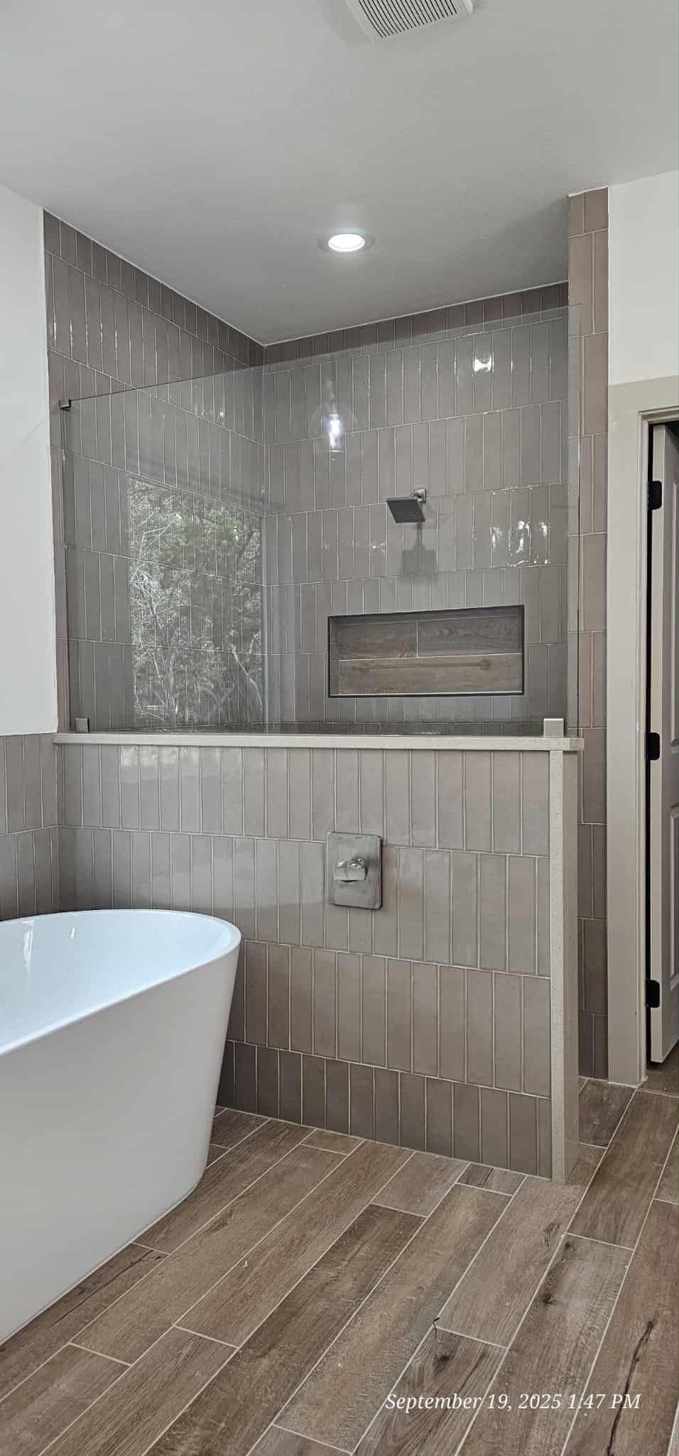 A modern bathroom with a white tub, walk-in shower with gray tiles and wooden flooring.