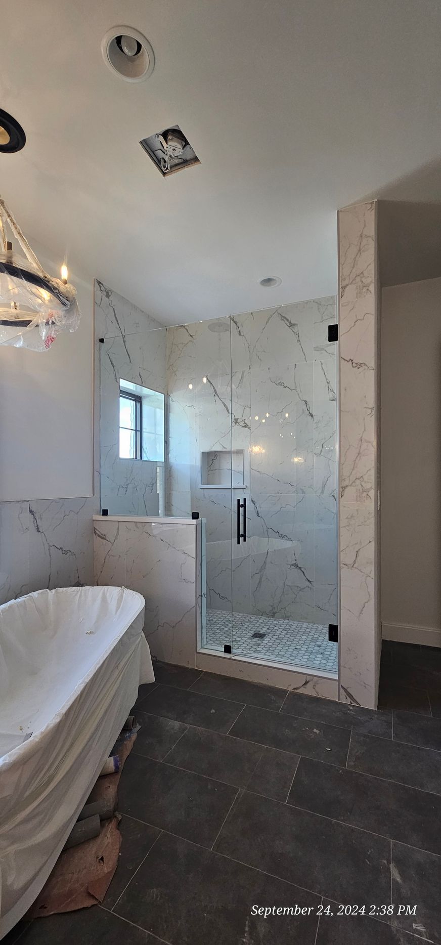 Bathroom with a glass shower, marble tile, and a bathtub.