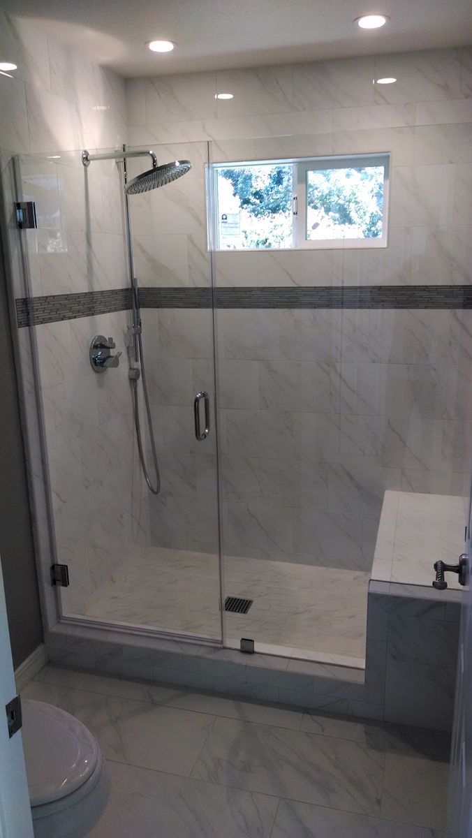Modern bathroom with glass shower enclosure, white marble tile, and small window.