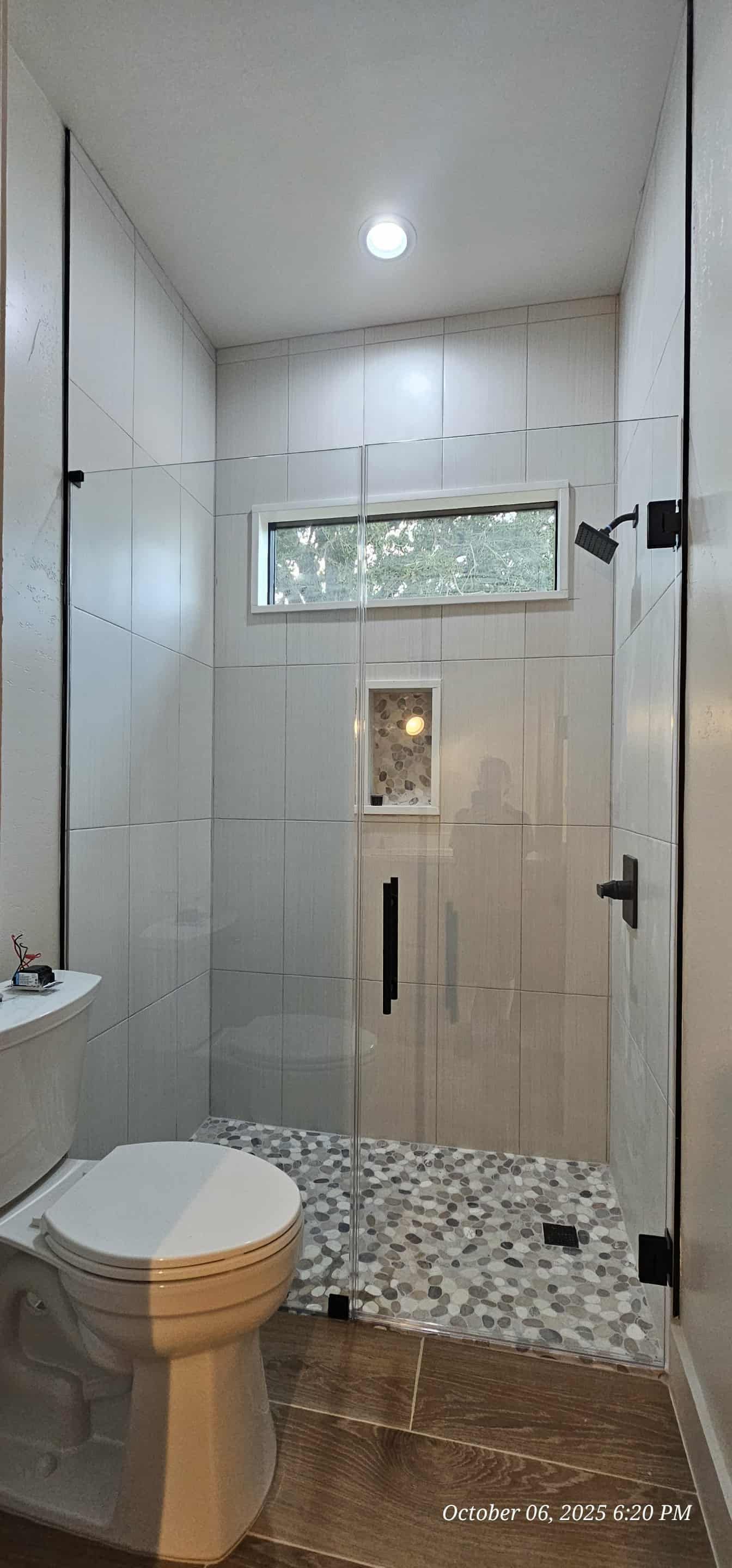 Bathroom with walk-in shower, toilet. Pebbled shower floor, stone tile floor. White walls with glass shower door.
