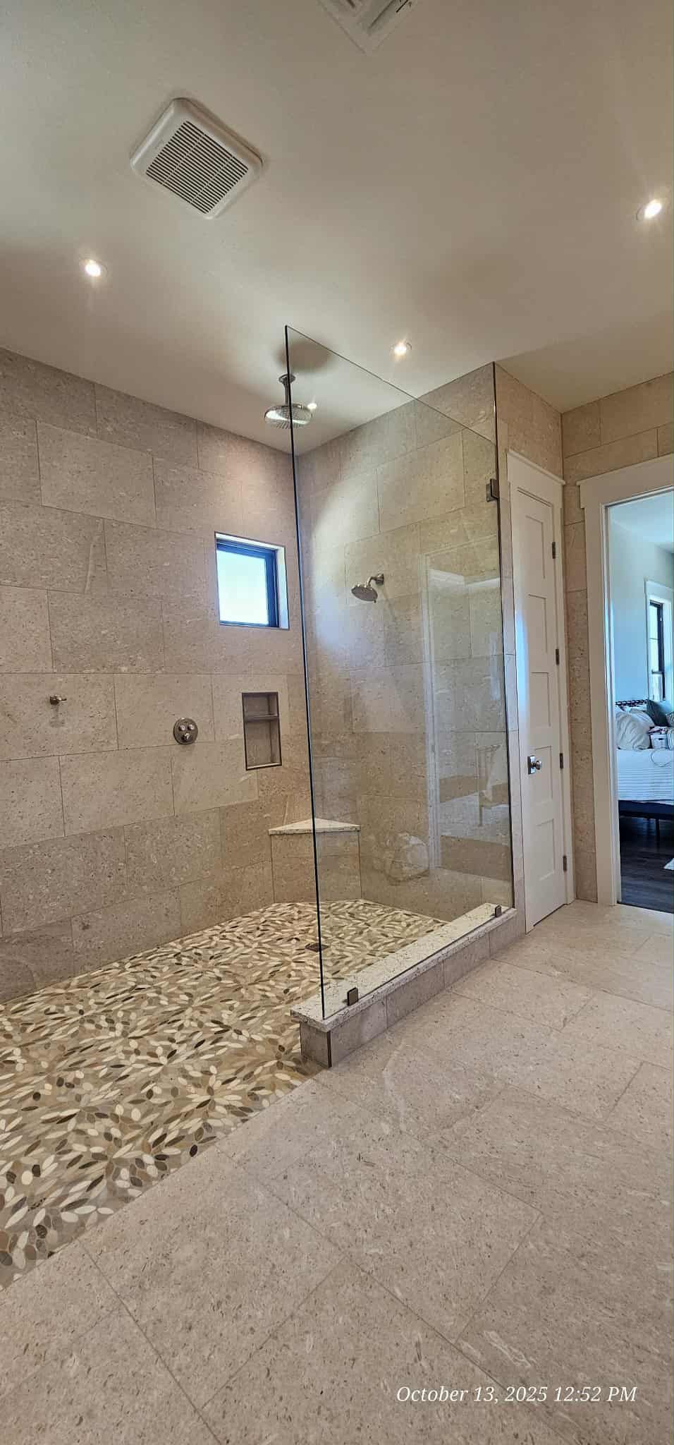 A modern bathroom with a pebble-floored shower, glass walls, and a recessed shelf.