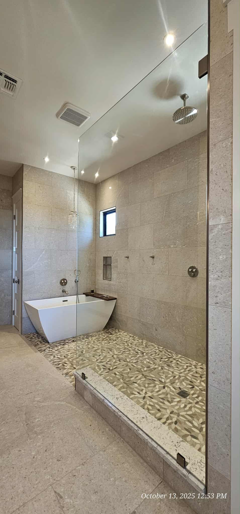 Luxurious bathroom with a stone pebble shower floor, a white tub, and neutral-colored tile walls.