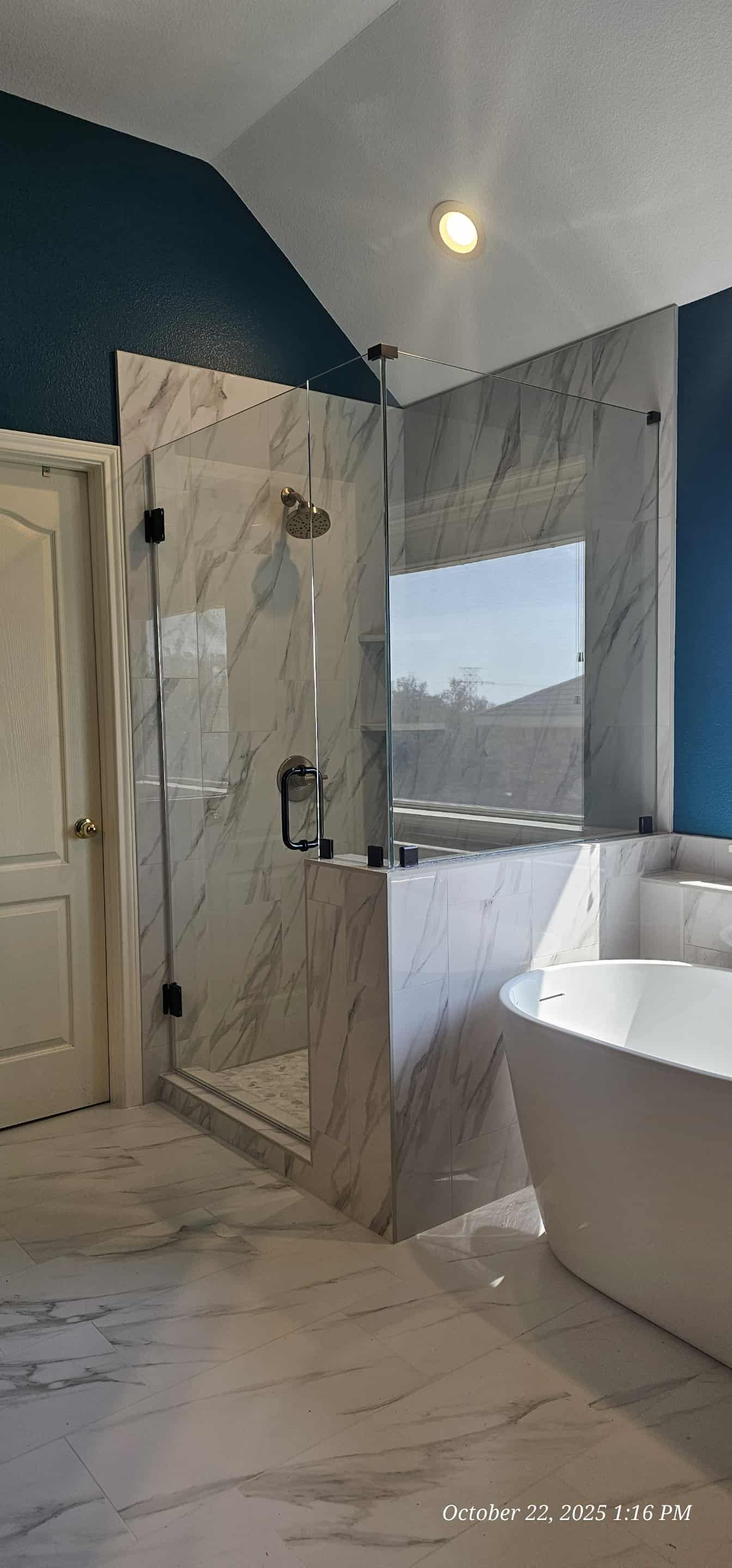 Bathroom with glass shower, white marble walls and floor, and a white soaking tub. Blue accent walls.