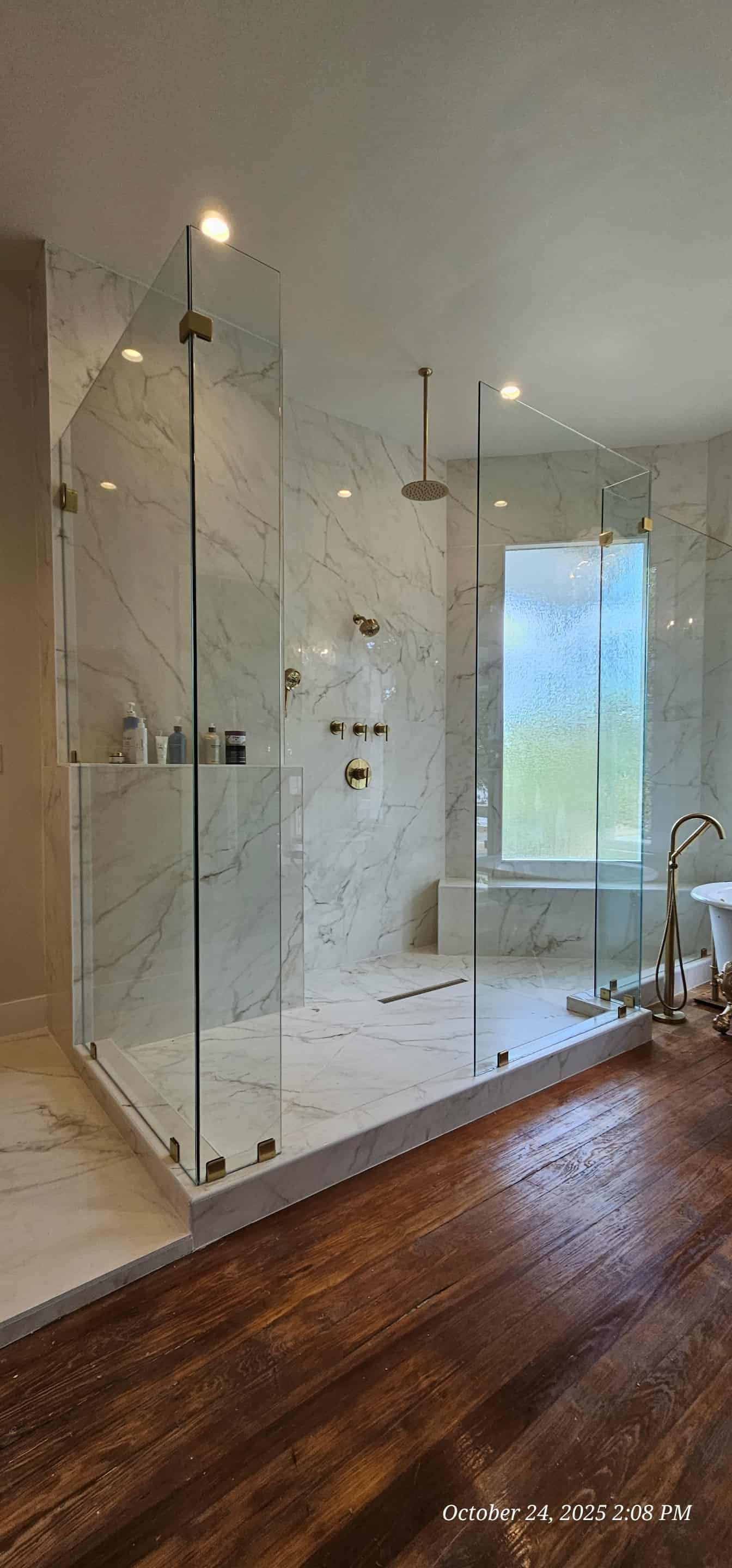 Modern bathroom with glass shower, light grey stone tile, skylight, black fixtures, and white towels.