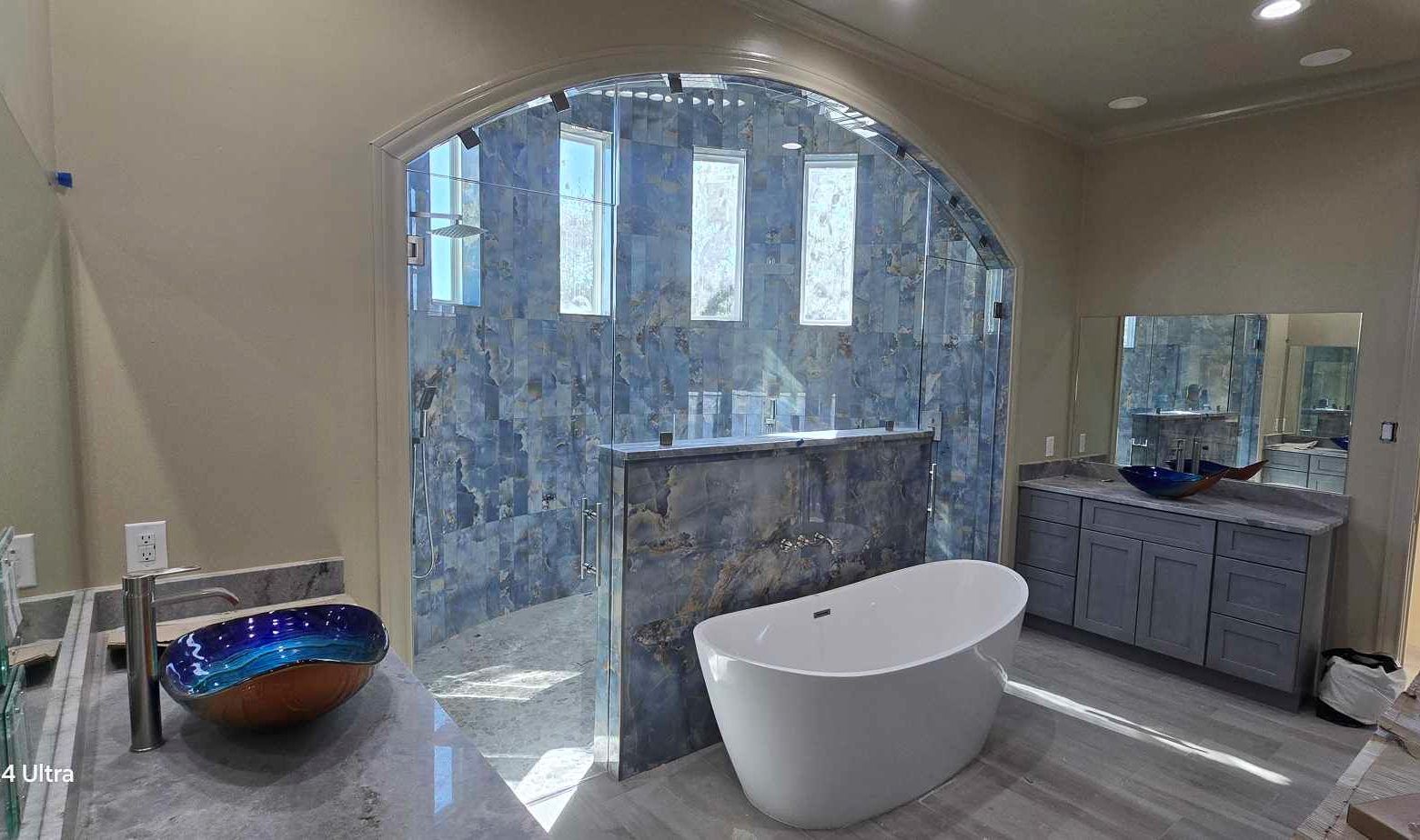 Bathroom with freestanding tub, stone wall shower, blue vessel sinks, and gray vanity.