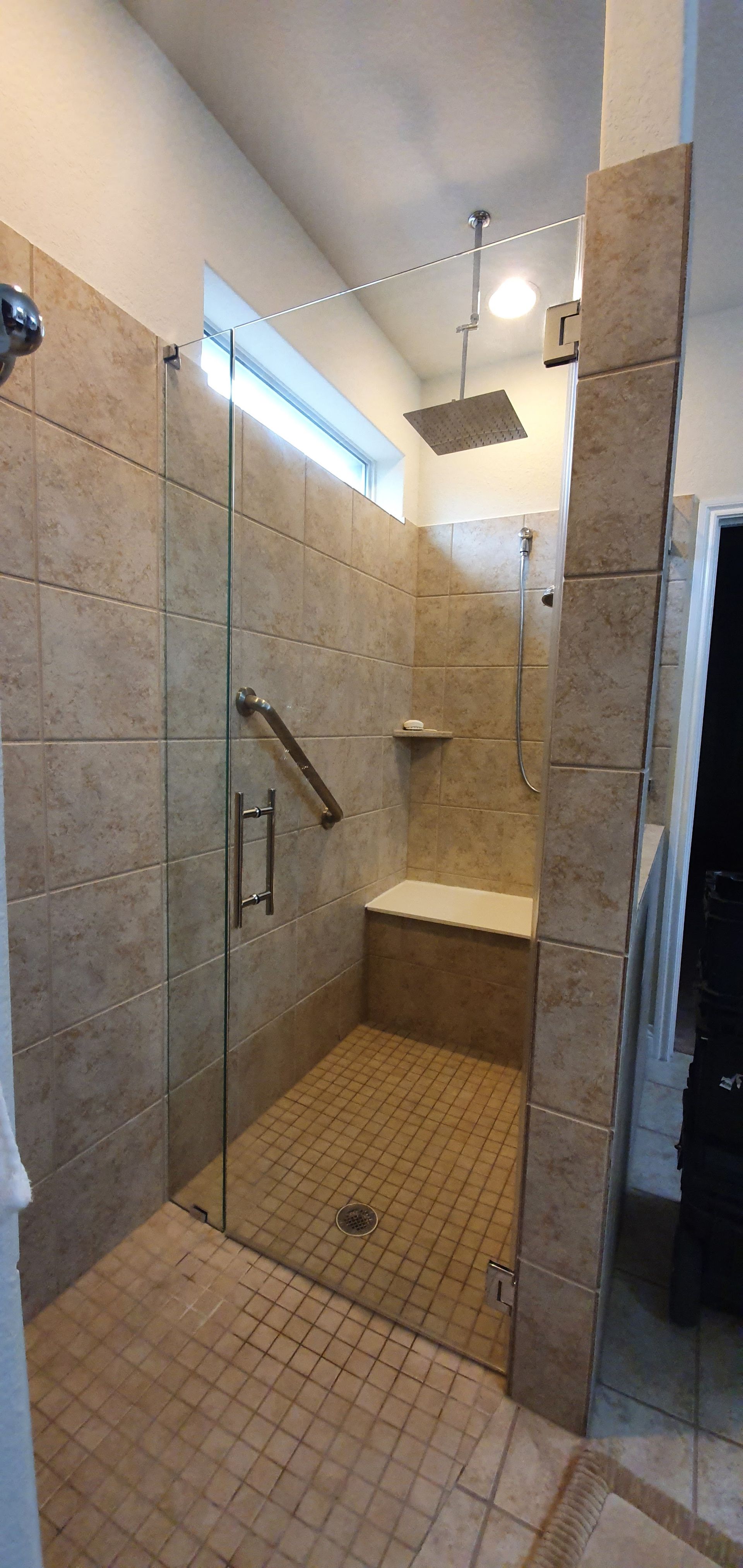 A spacious walk-in shower with stone tile walls, a glass door, and a built-in bench.