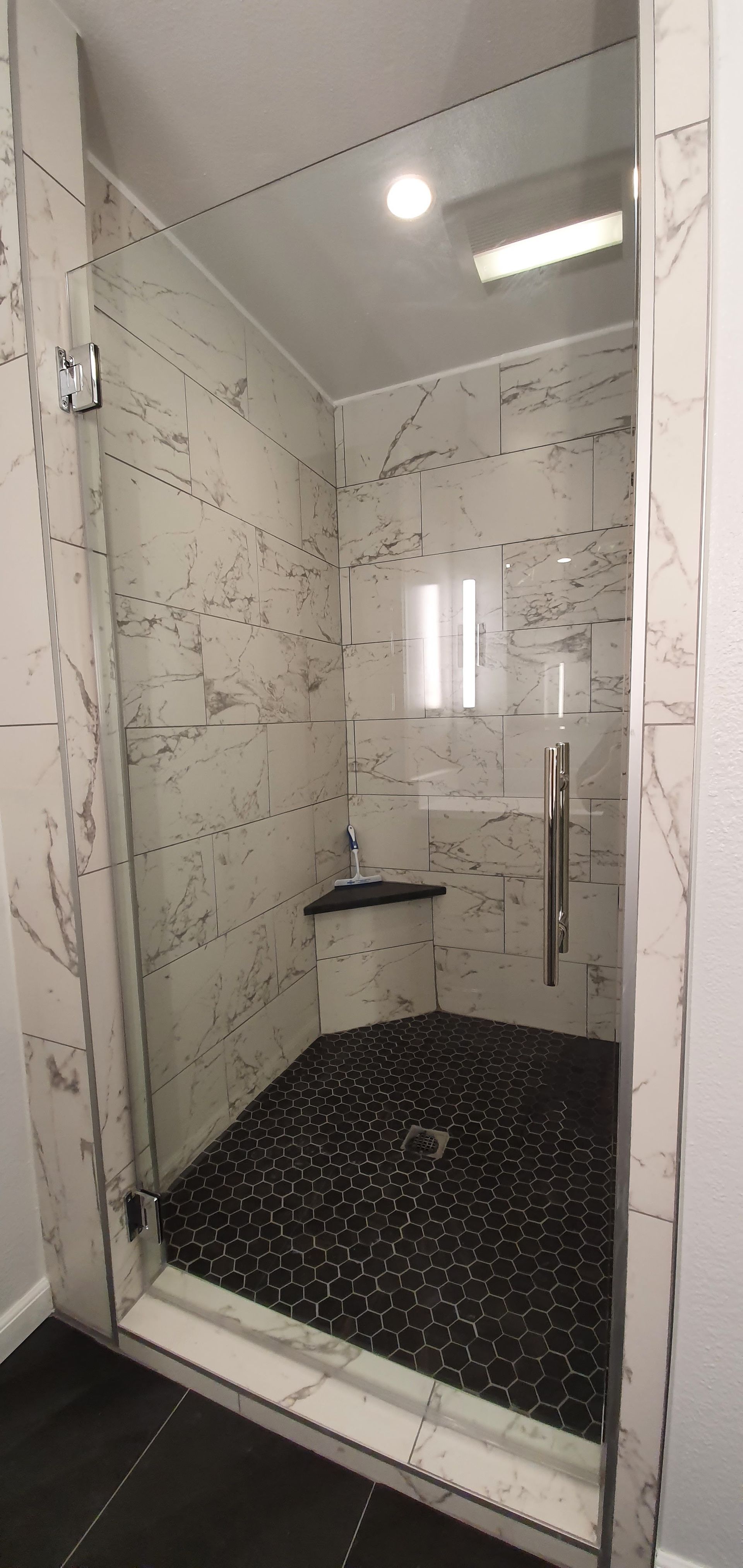 Shower with black pebble floor, white marble tile walls, and glass door.