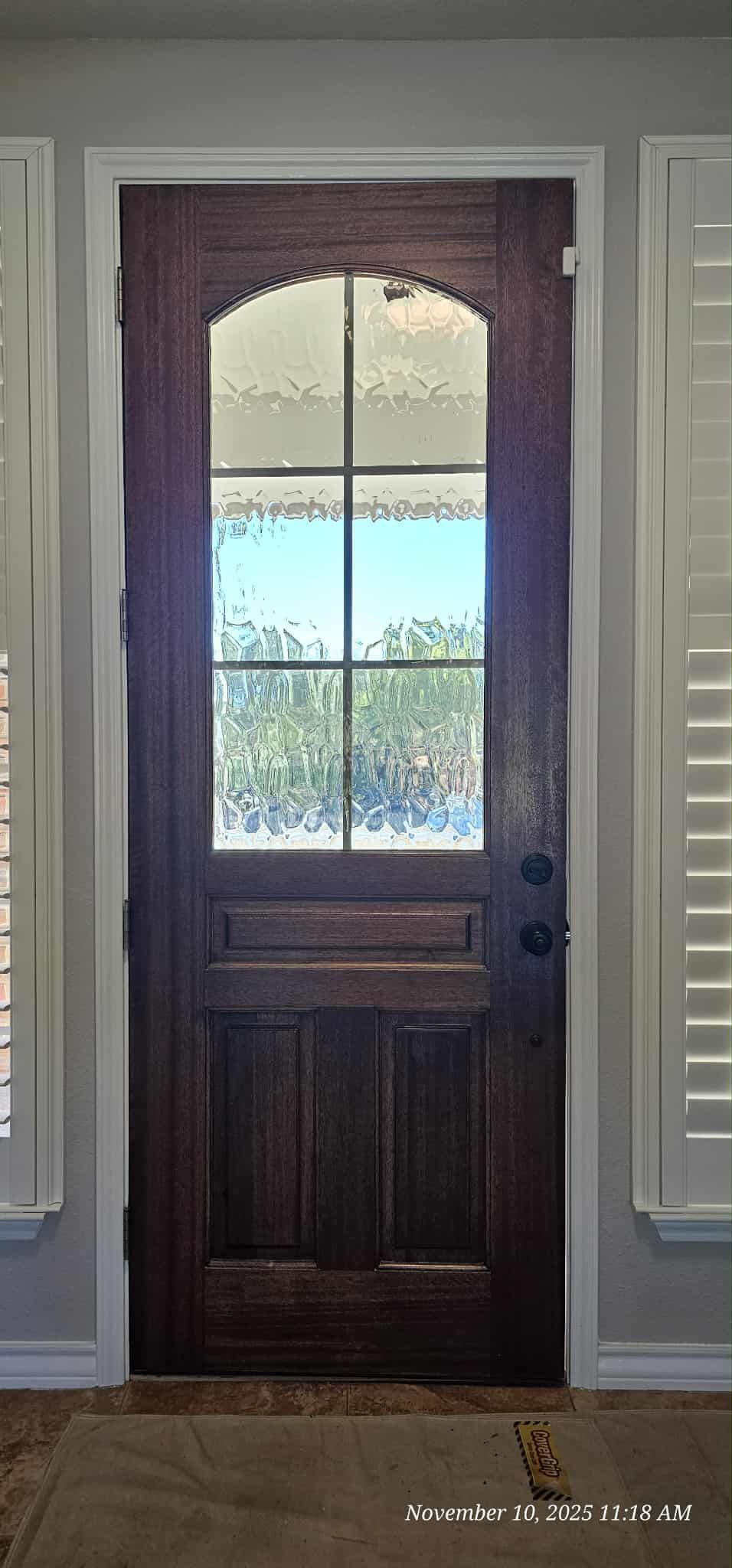 Dark wooden front door with arched glass panels, flanked by white shutters.