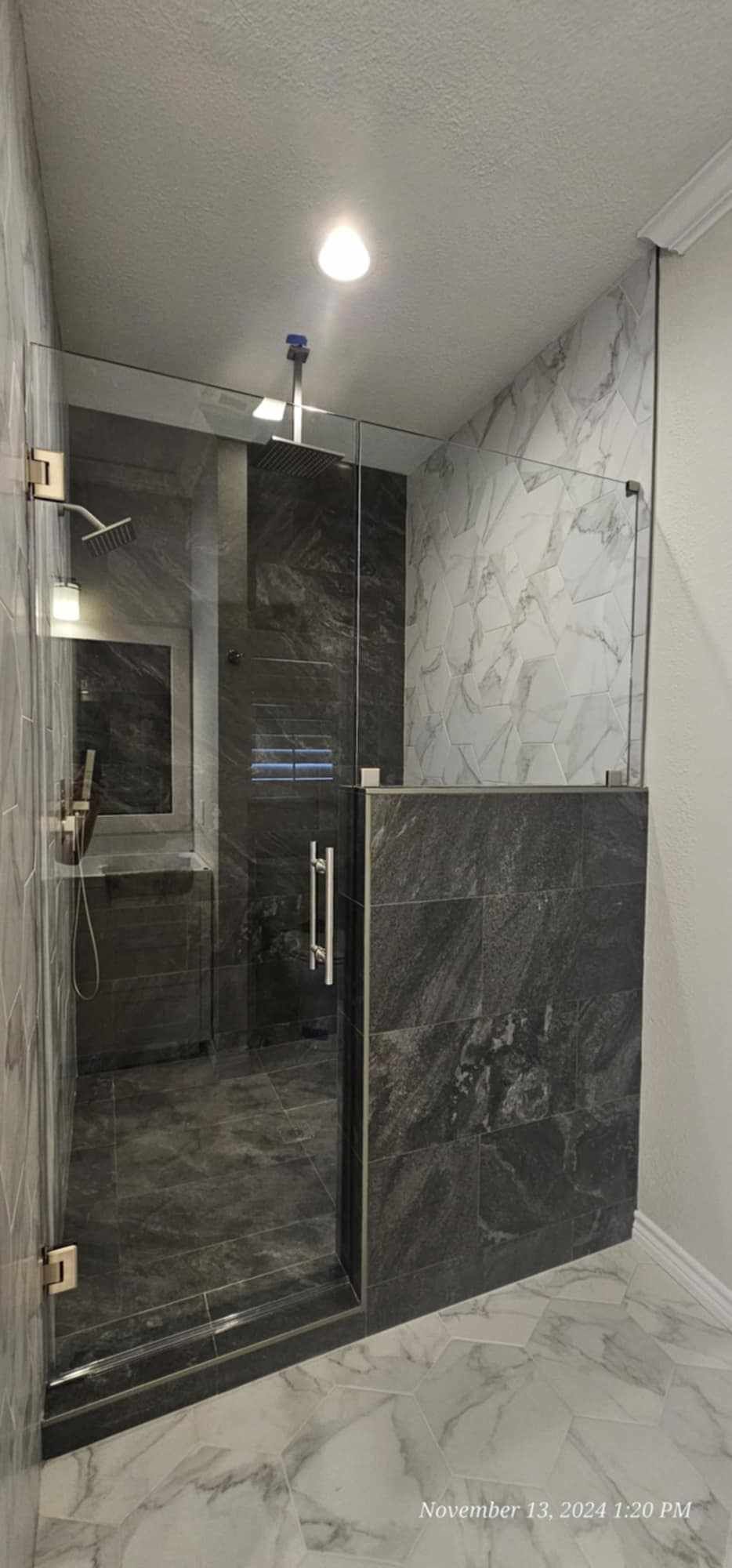 A luxurious shower with dark tile and marble floors, framed by glass doors and walls.