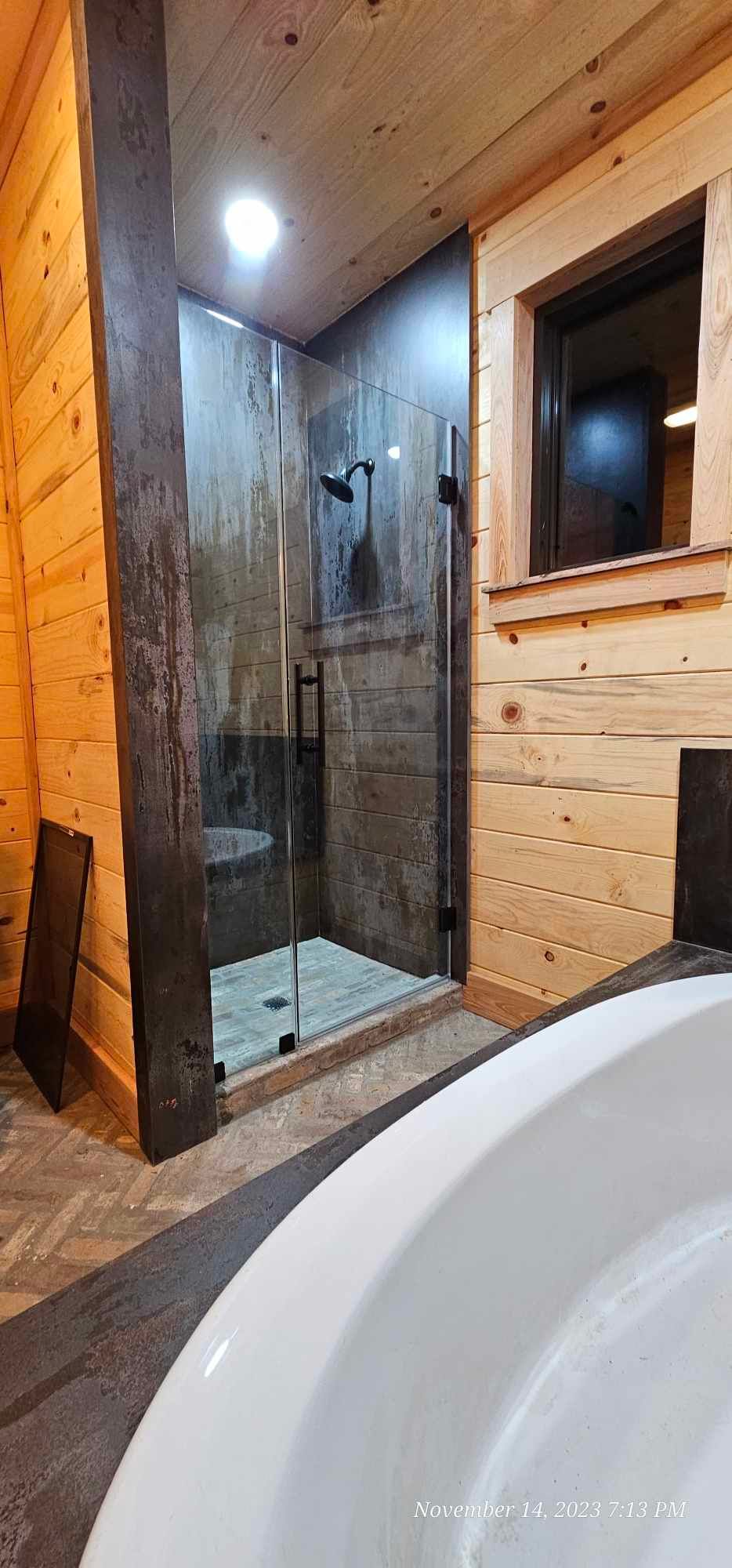 Bathroom with wooden walls, glass shower, and white tub.
