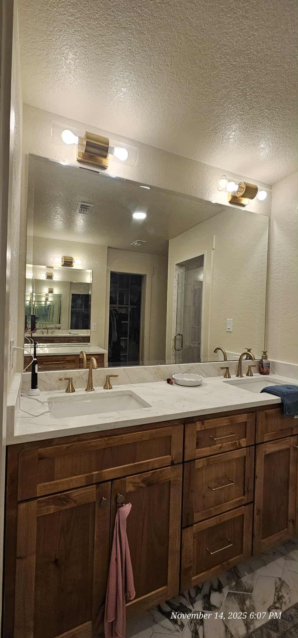 Bathroom with a large mirror above a double vanity with brown cabinets and a white countertop.