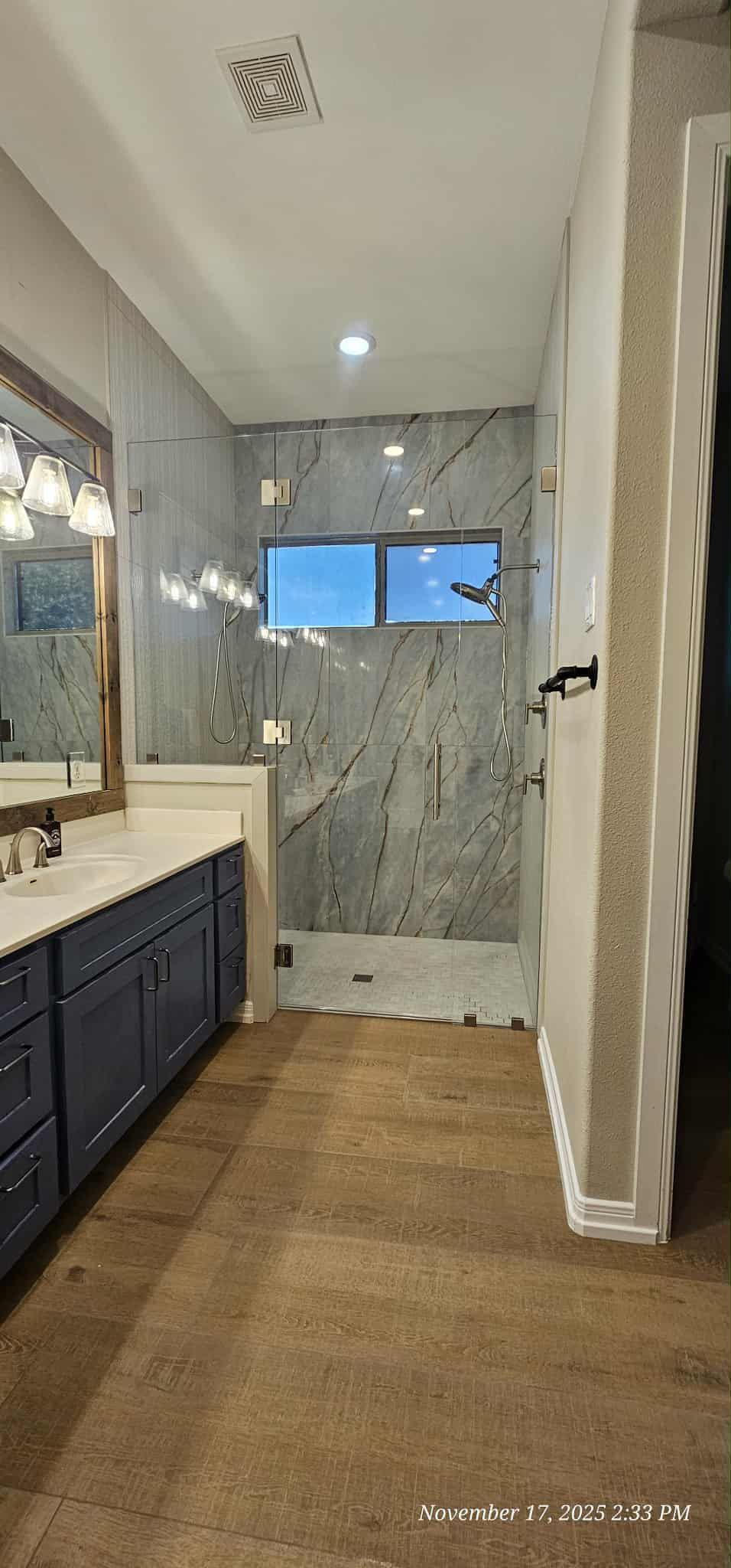 Bathroom interior with blue cabinets, a tiled shower, and a stone floor.