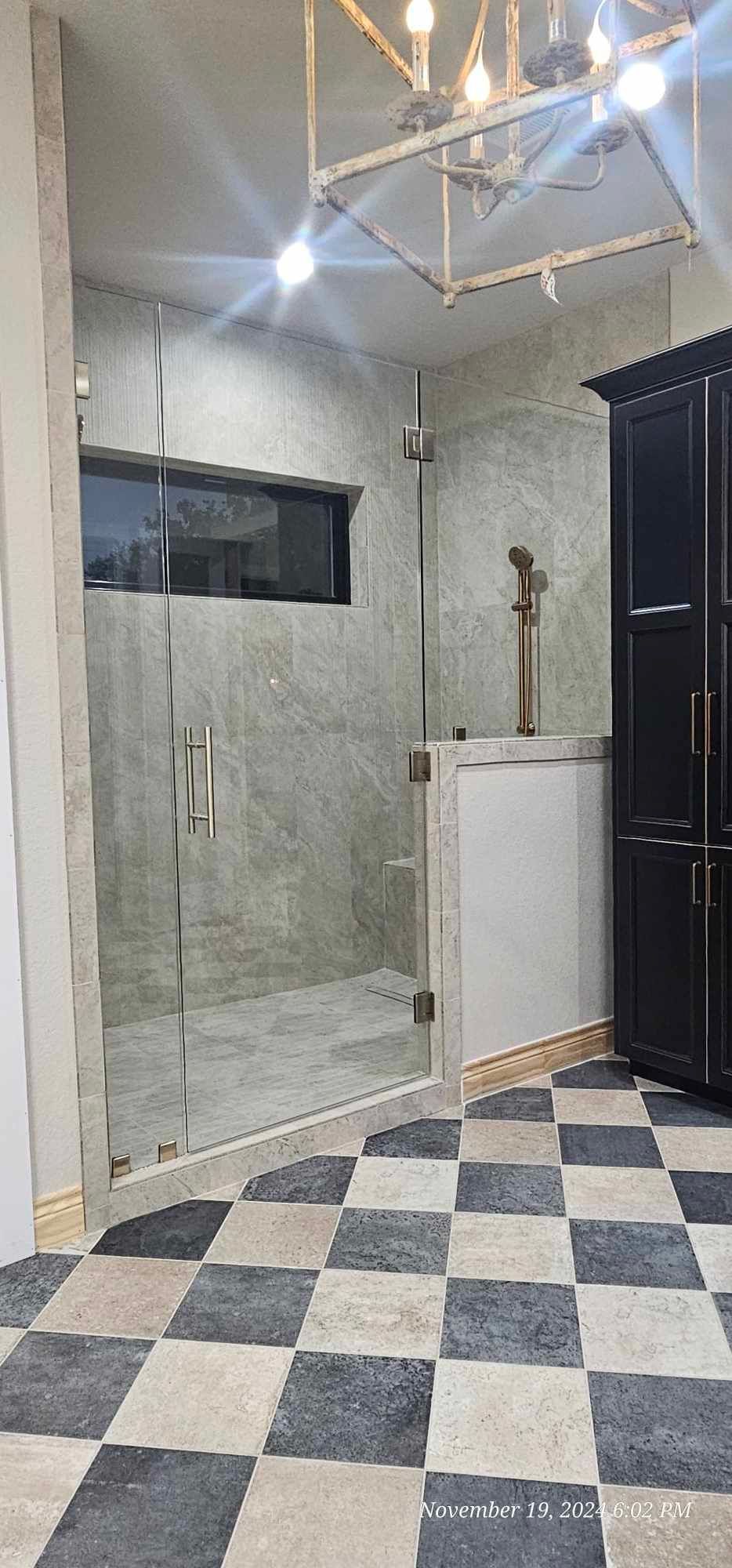 Bathroom with checkered floor, glass shower, black cabinet, and a chandelier.