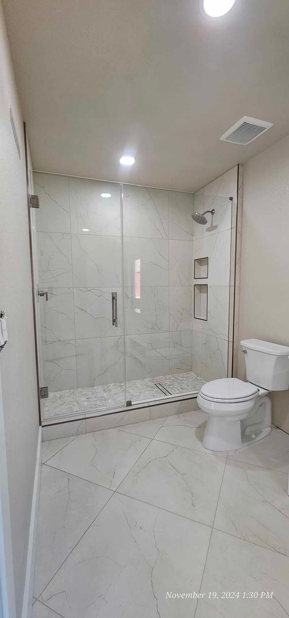 A modern white bathroom with a glass shower, white toilet, and tile flooring.