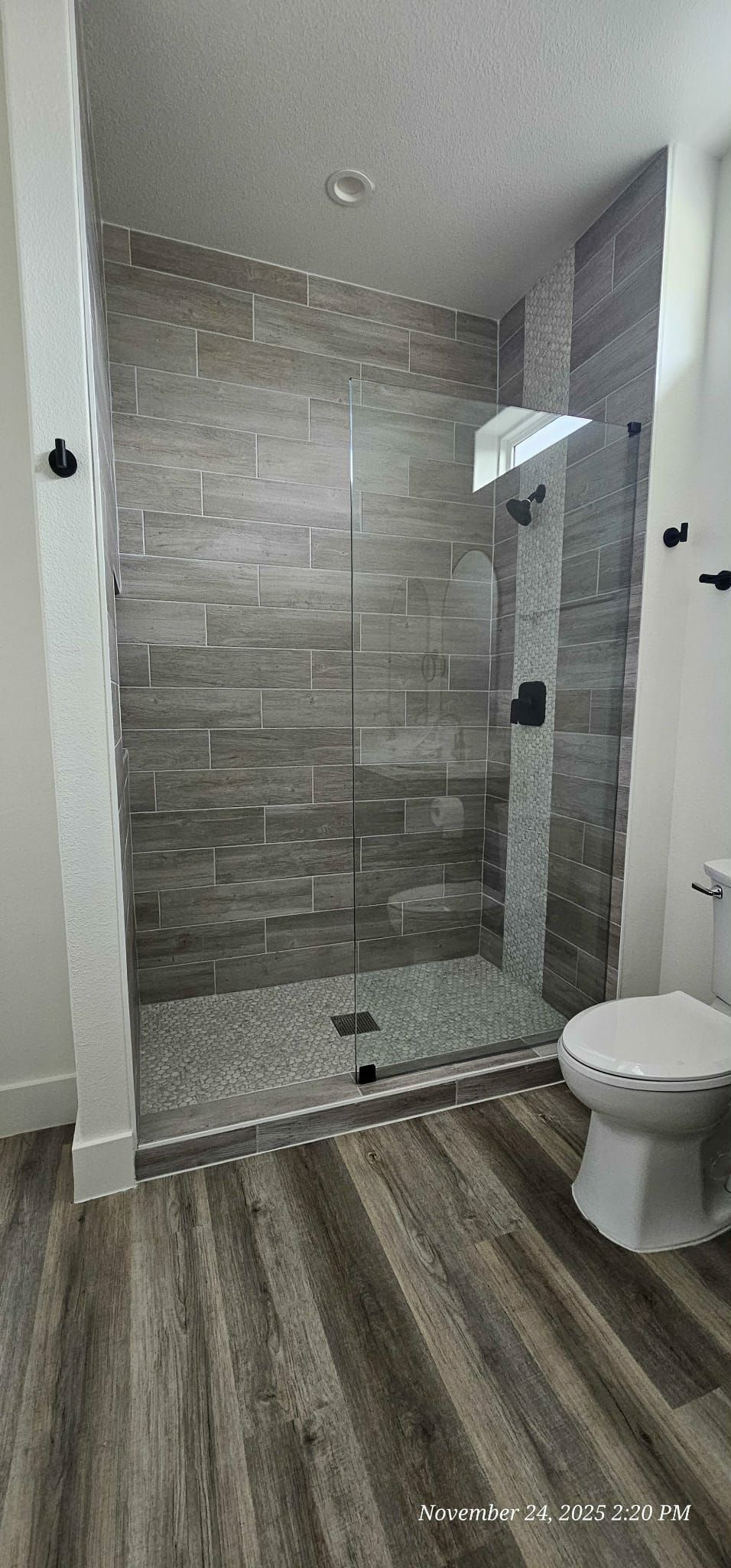 Bathroom with tiled shower and glass door, next to a toilet. Wooden floor.