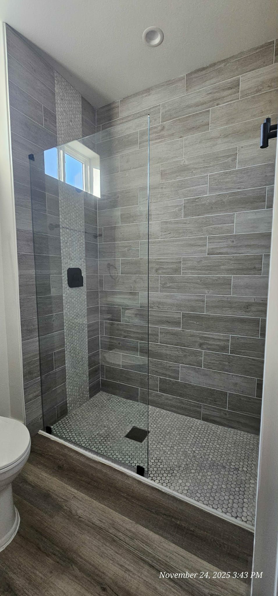 A modern shower with gray tile, a clear glass door, and pebble flooring.