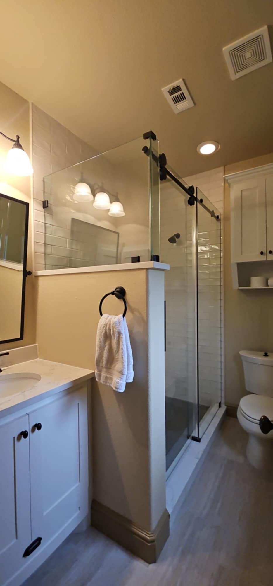 Bathroom with a walk-in shower. White cabinetry, glass shower door with black hardware, and gray tile flooring.