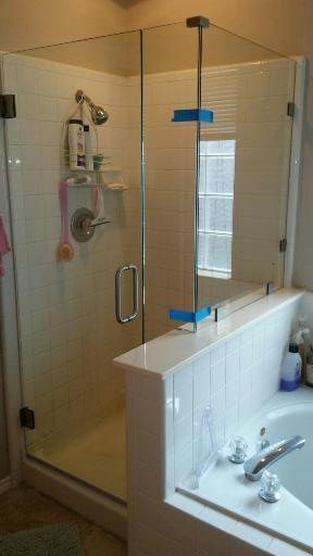 Glass shower enclosure next to a bathtub; white tile, chrome fixtures, toiletries visible.