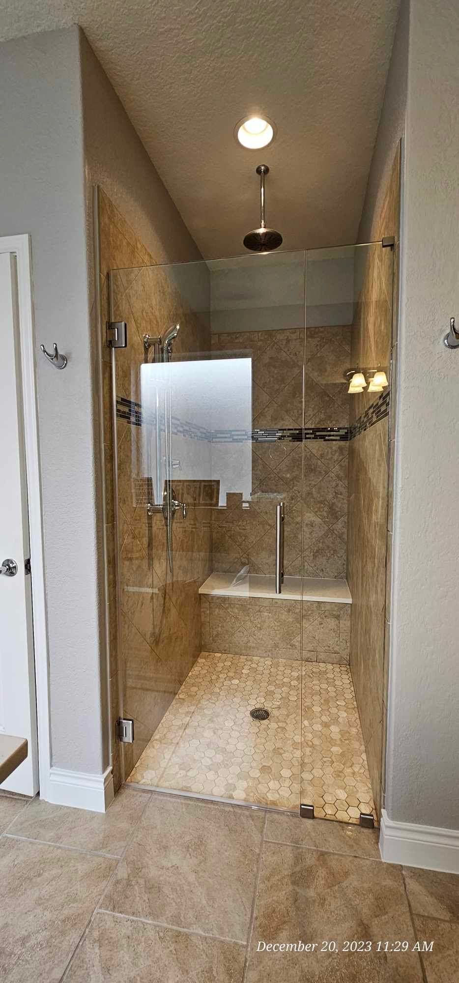 Bathroom with glass shower door, pebble floor, and stone walls.
