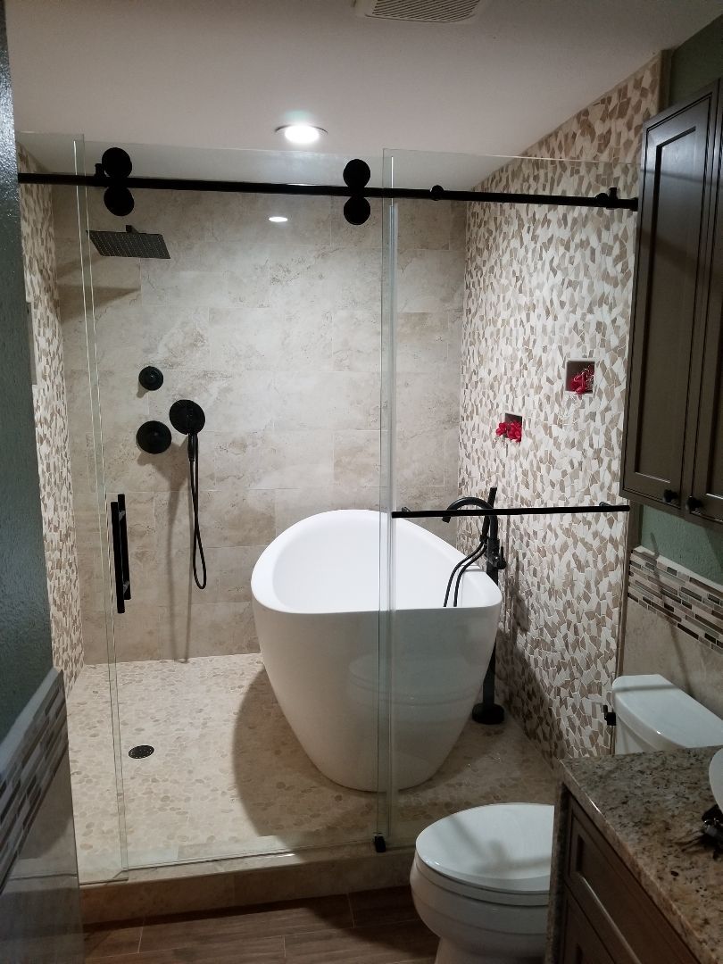 Bathroom with freestanding tub, glass shower enclosure, and dark fixtures against stone tile.