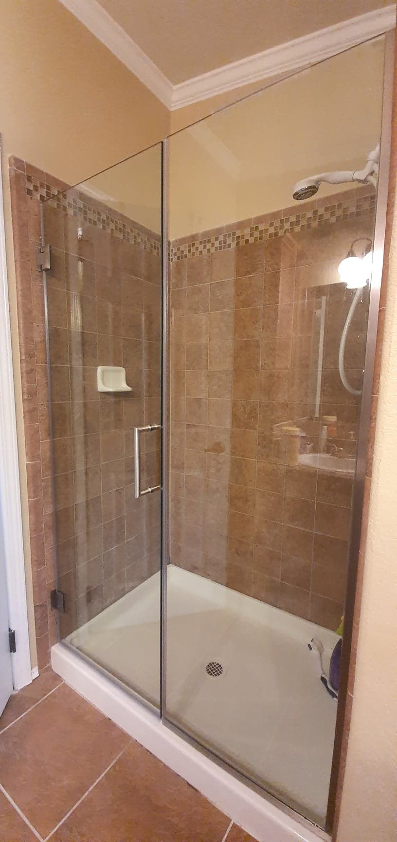 A shower with brown tile walls, a white shower base, and a glass door.
