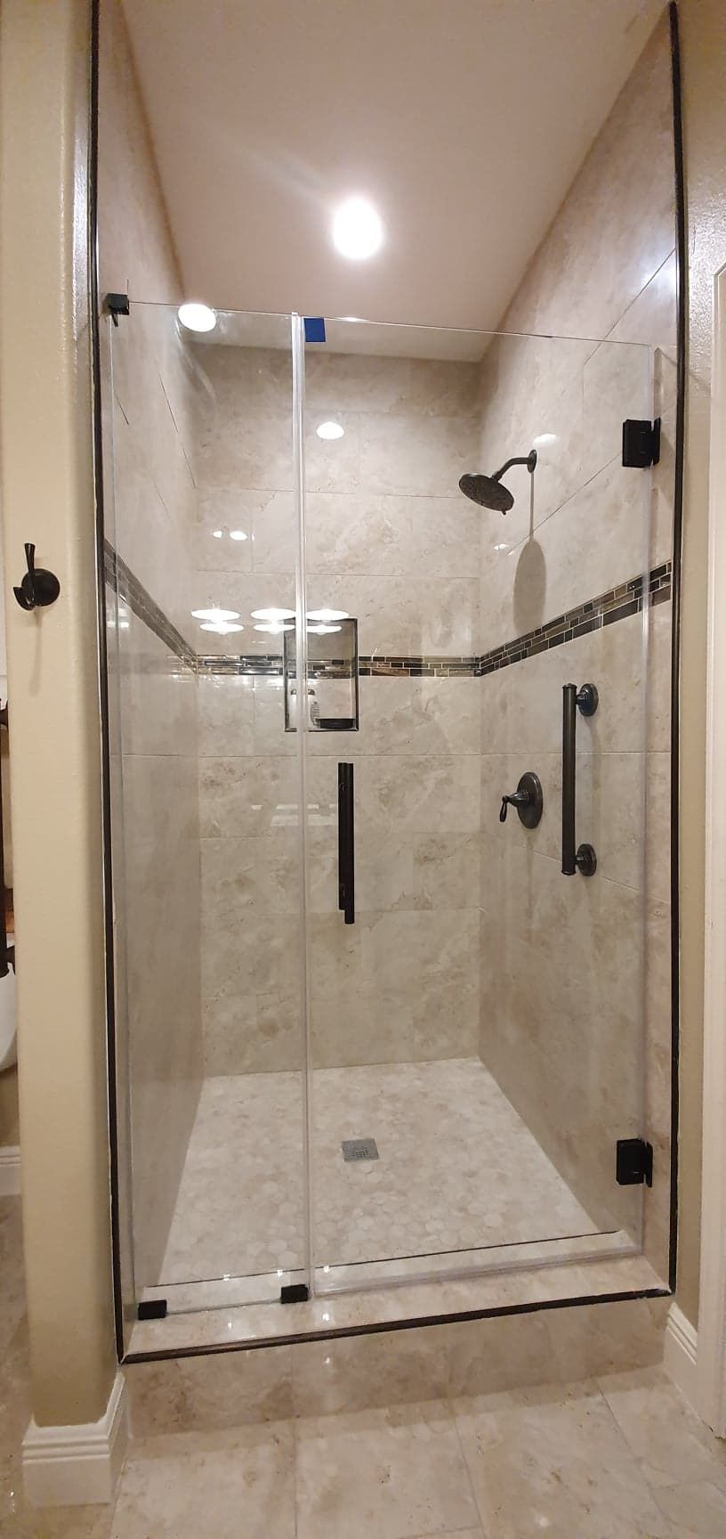 A glass shower enclosure with black hardware, beige tile walls and flooring, and a shower head.
