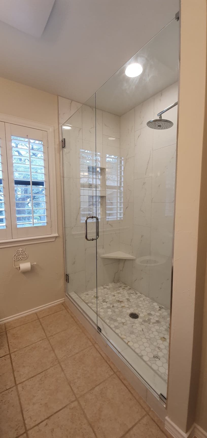 A modern shower with clear glass doors, white tiled walls, and pebble flooring.